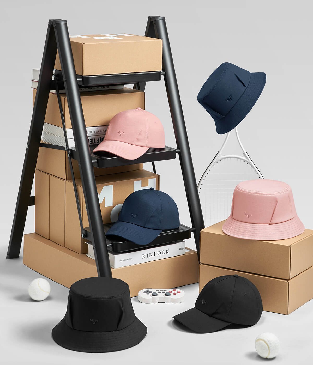 Stylish pink, navy, and black bucket hats and caps displayed with books, tennis racket, and game controller