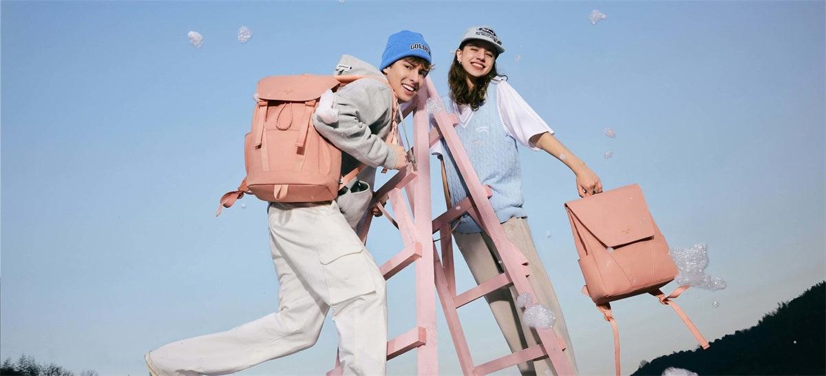 Two models with pink backpacks and handbags on a ladder outdoors, bubbles floating around
