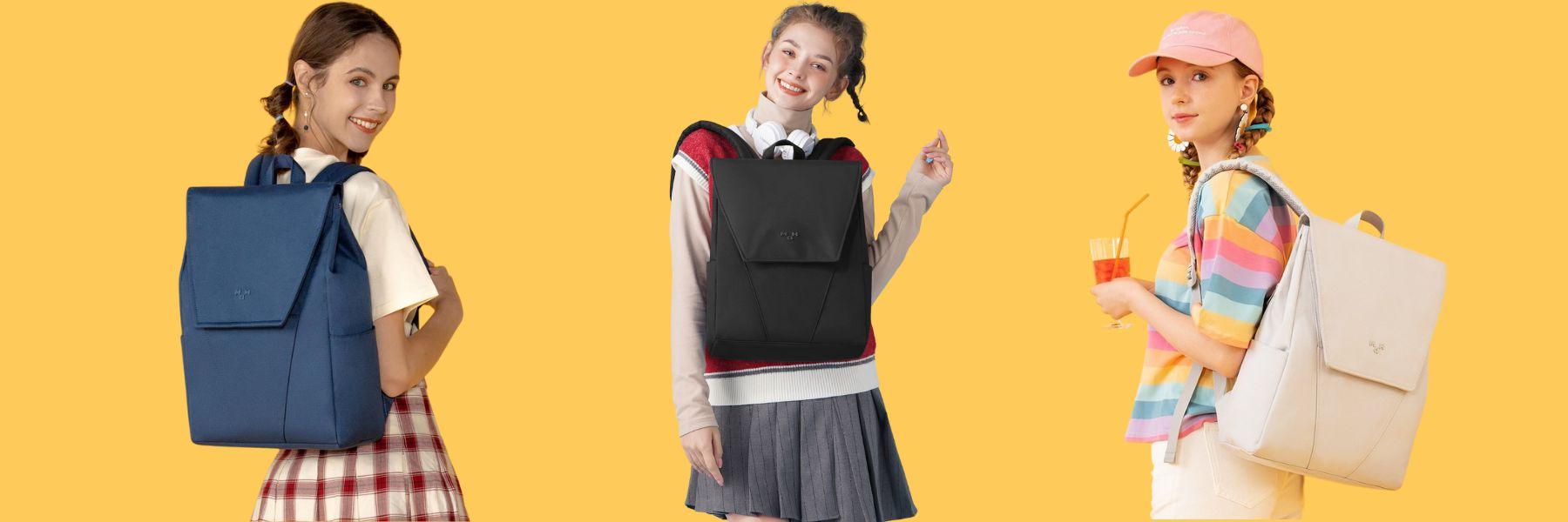 Three girls modeling stylish backpacks in blue, black, and beige against a yellow background