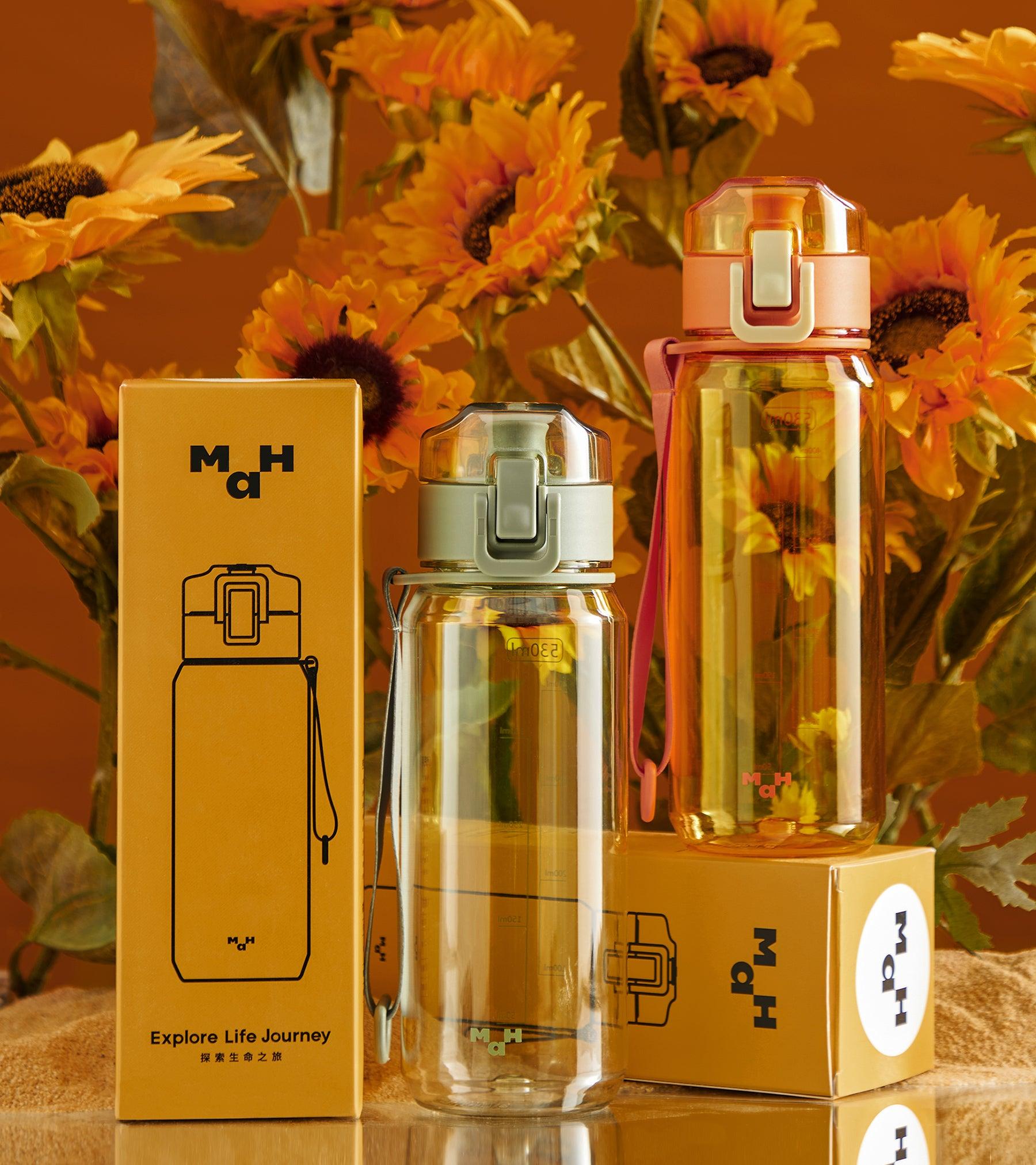 Clear reusable water bottles with flip lids and carry straps, shown with packaging against sunflower backdrop