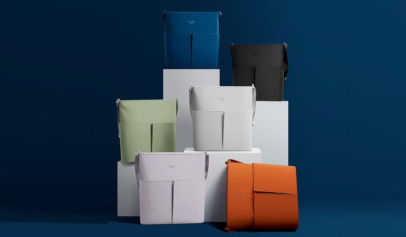 Modern minimalist bags in blue, green, white, black, and orange displayed on white pedestals