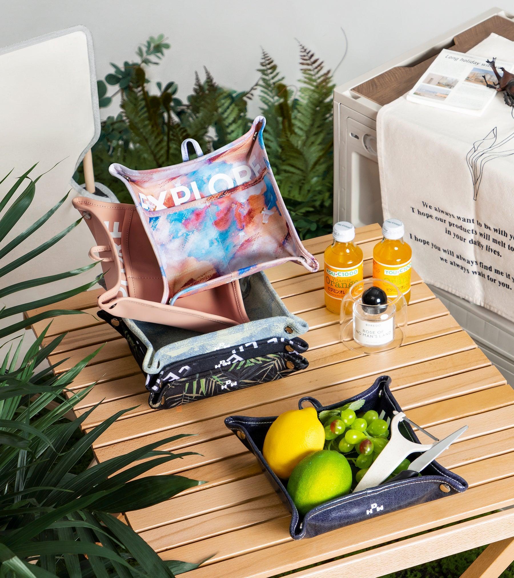 Colorful 'EXPLORE' print foldable tote bags on wooden table with fruit, drinks, and greenery for lifestyle use