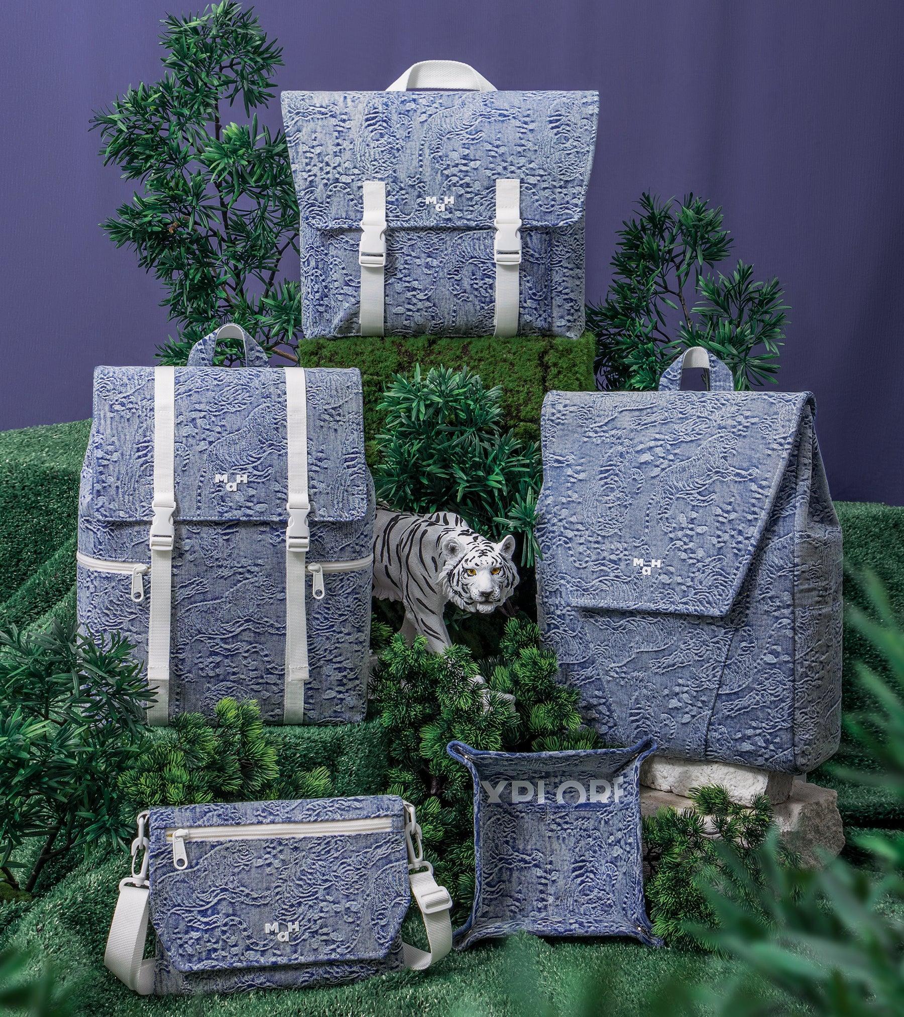 Blue tiger-print backpacks and bags with white straps, styled with greenery and a white tiger figurine.