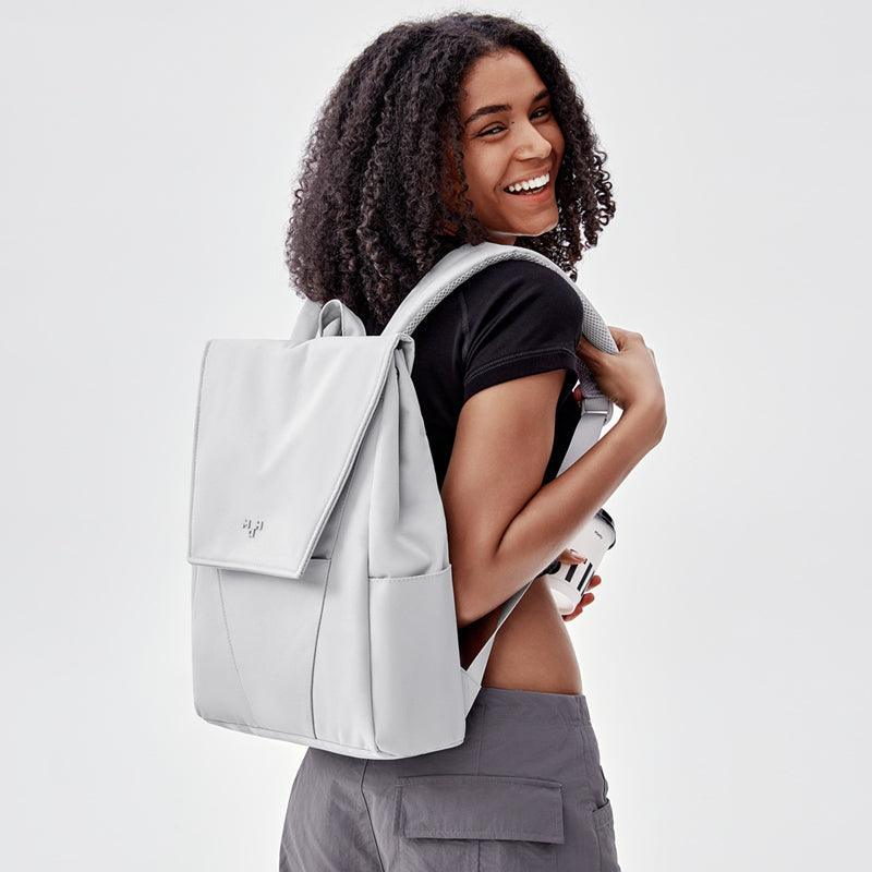 Stylish light gray backpack with front pocket, worn by smiling woman in casual outfit