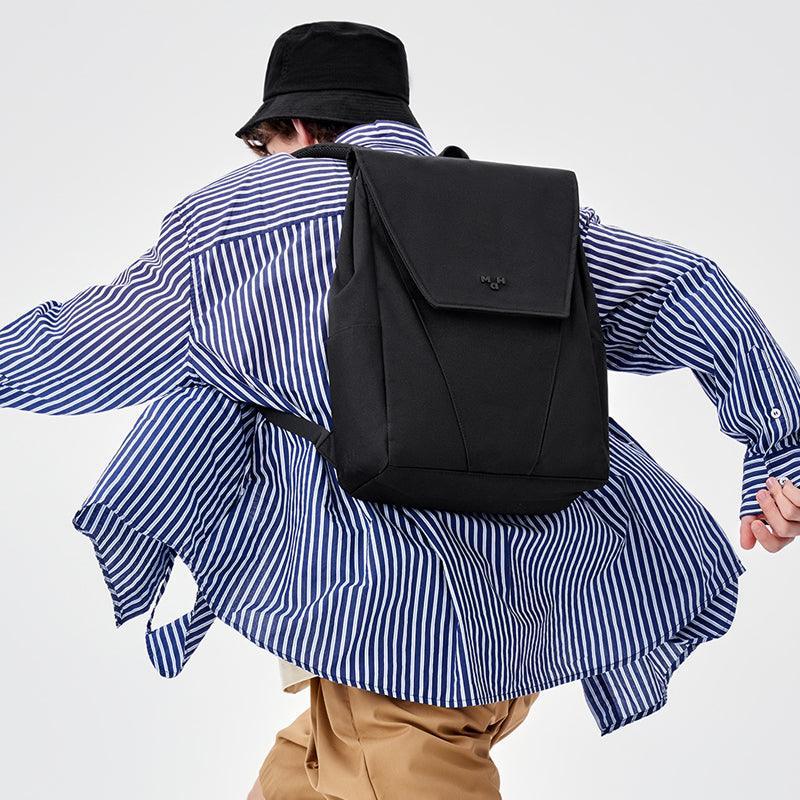 Black minimalist backpack worn by person in striped shirt and bucket hat, stylish urban accessory