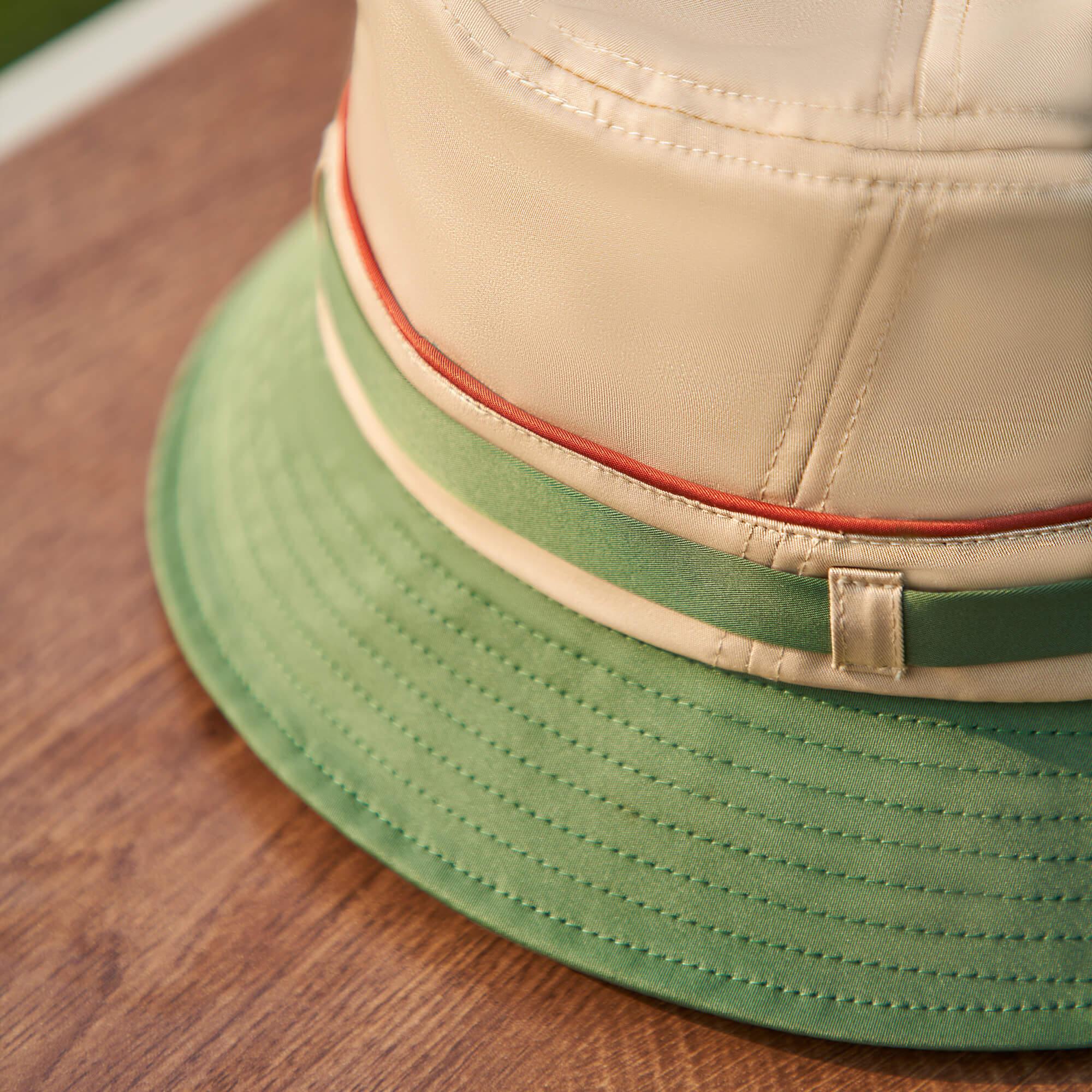 Beige and green bucket hat with red trim, detailed stitching, on wooden surface