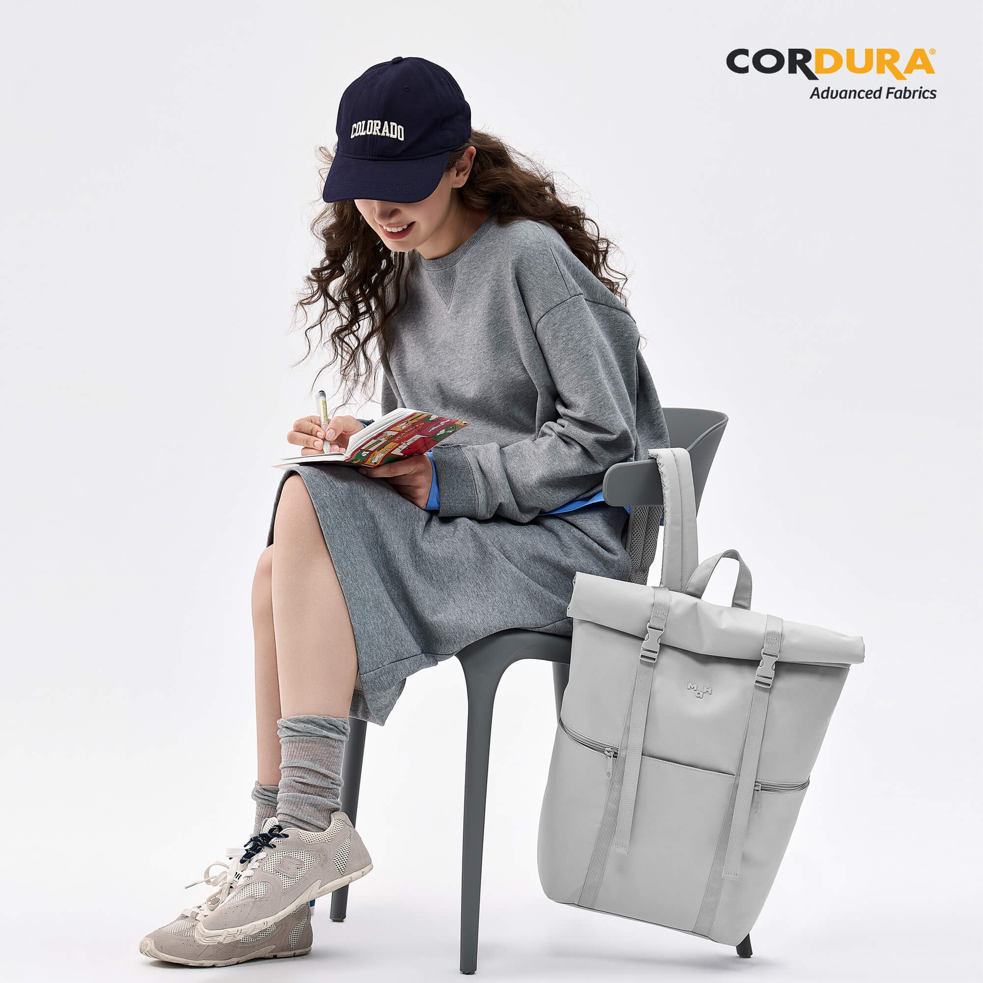 Woman writing in notebook with gray roll-top backpack, Cordura fabric, casual style