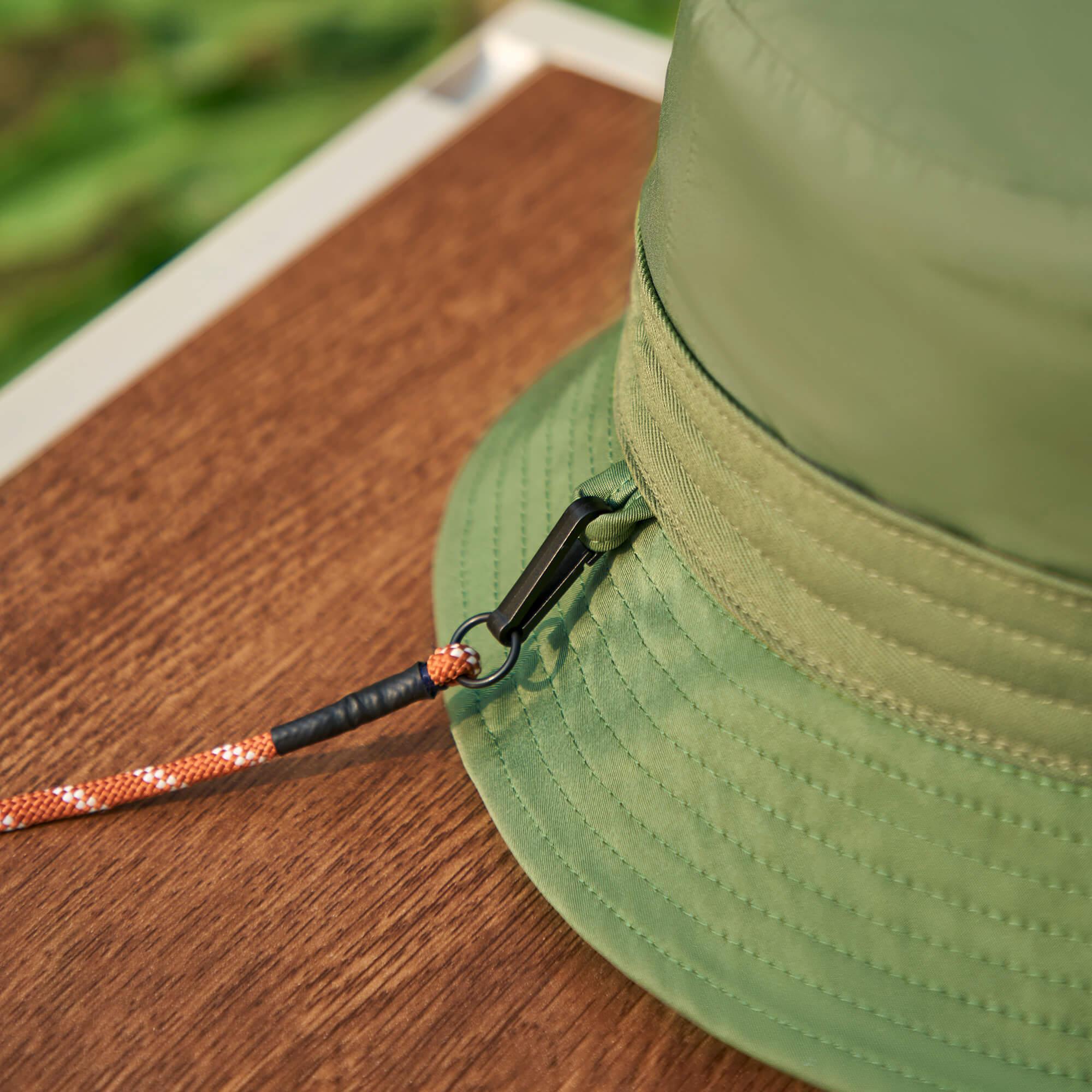 Olive green bucket hat with adjustable orange rope chin strap, resting on wooden surface