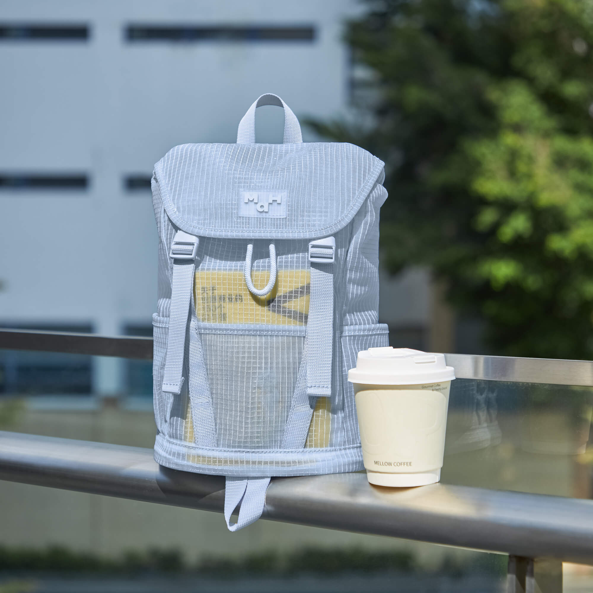 Light gray striped backpack with front pocket and coffee cup on railing, ideal for daily commutes and urban lifestyle