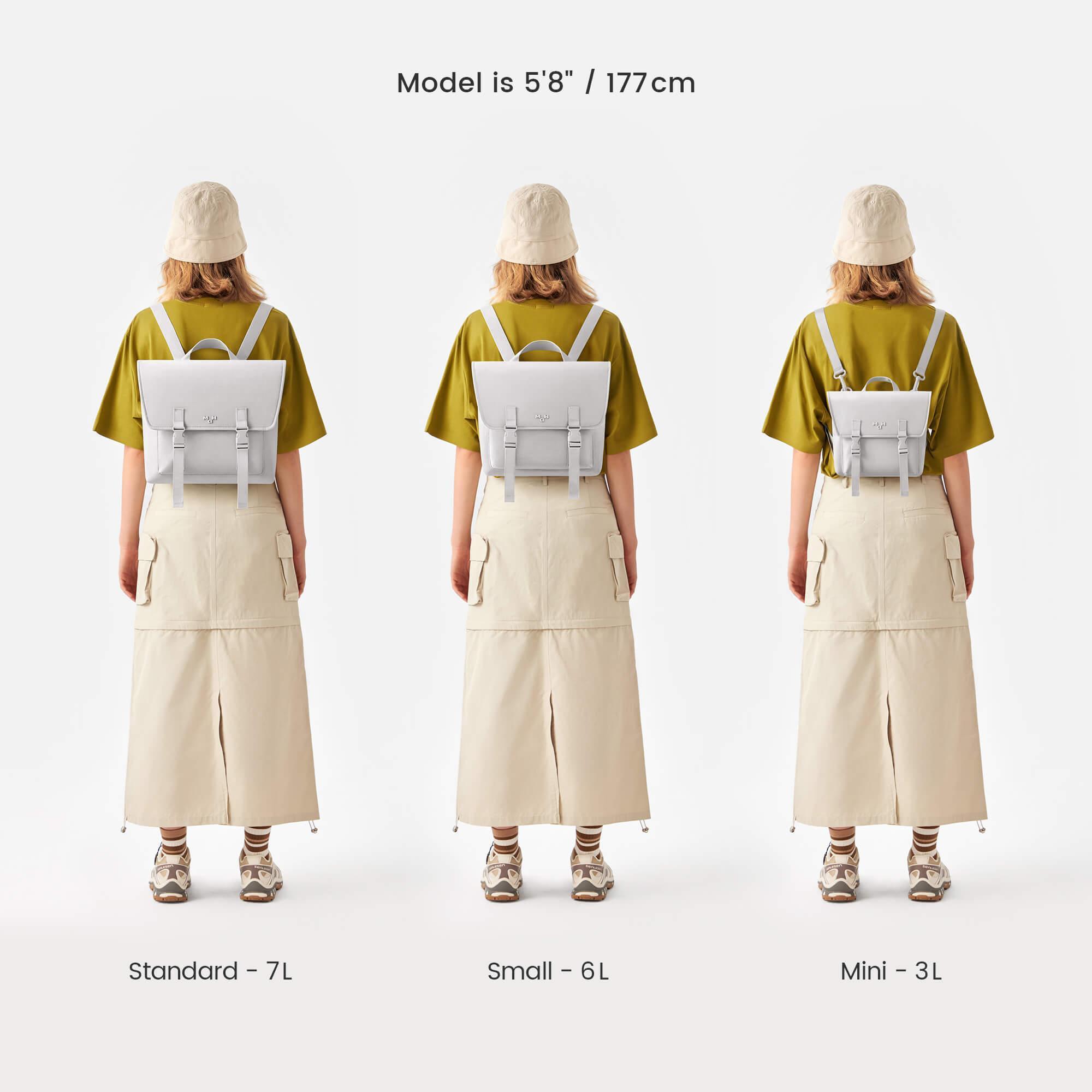 Three sizes of minimalist white backpacks: Standard 7L, Small 6L, Mini 3L, worn by model in olive tee and beige skirt.