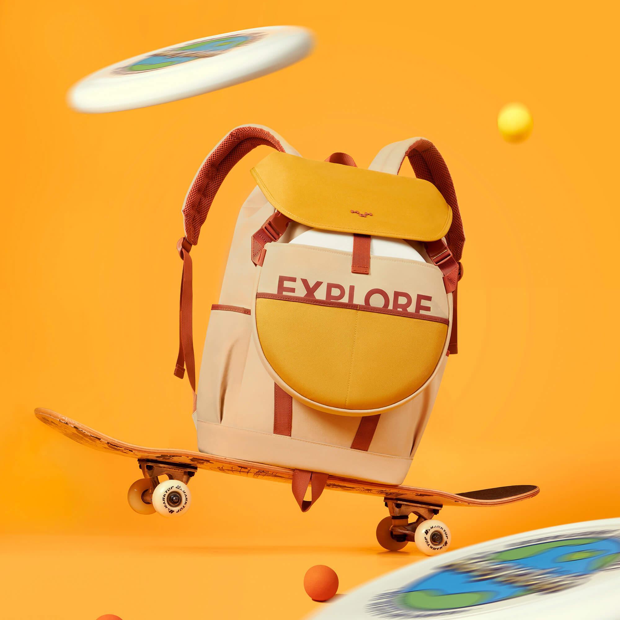 Explore backpack on skateboard with frisbee, vibrant orange background, adventure lifestyle gear
