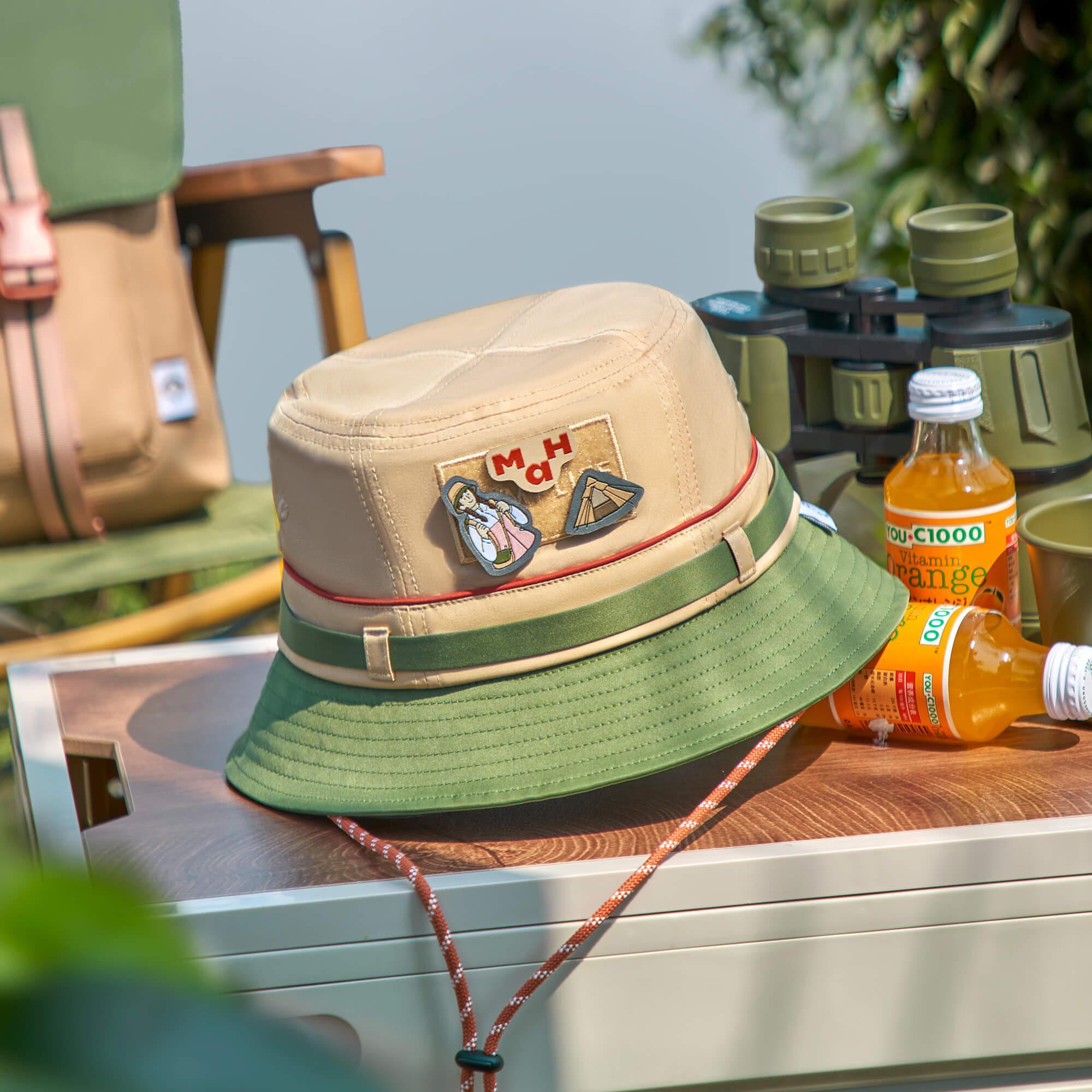 Beige and green bucket hat with adventure patches, perfect for outdoor travel and camping gear.