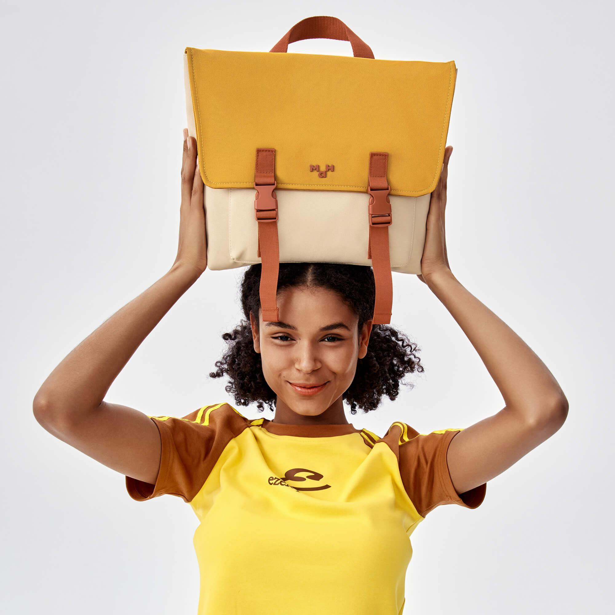 Woman holding mustard yellow and cream satchel bag with brown straps, stylish everyday accessory