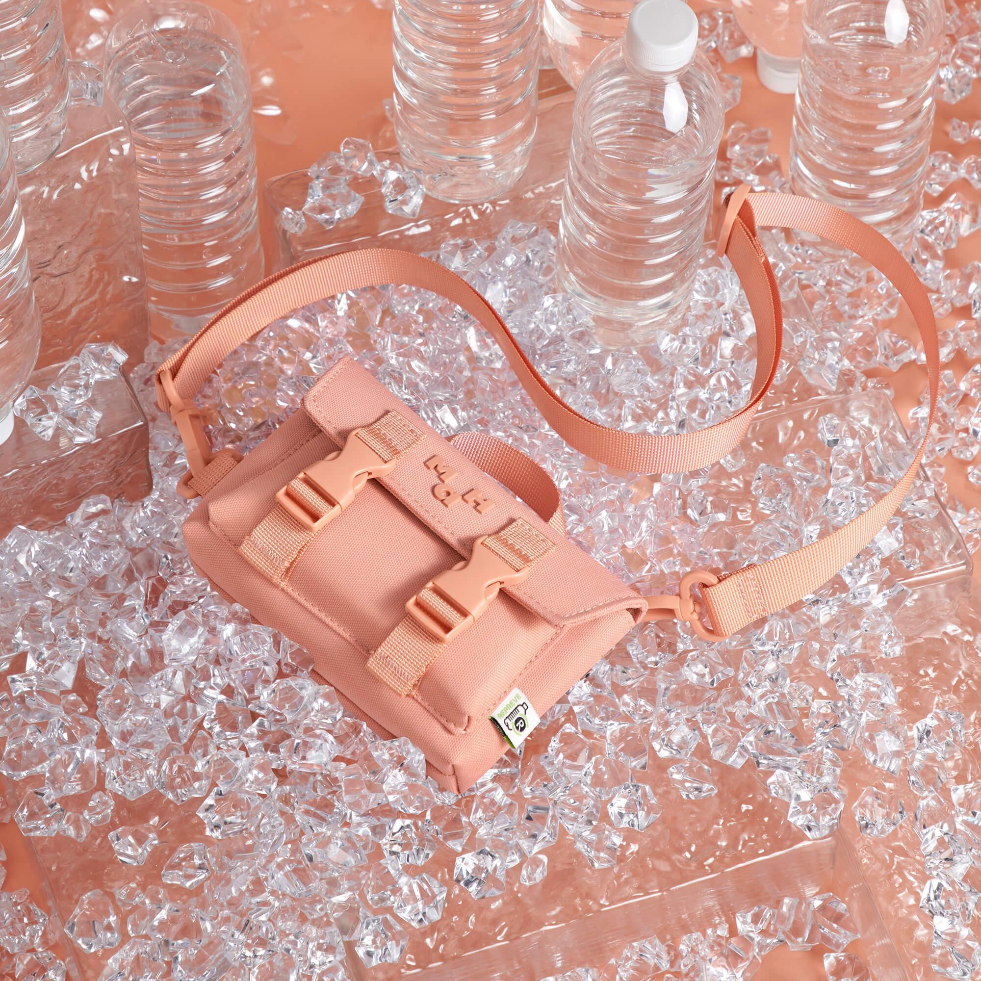 Peach crossbody bag with buckles on ice, surrounded by water bottles