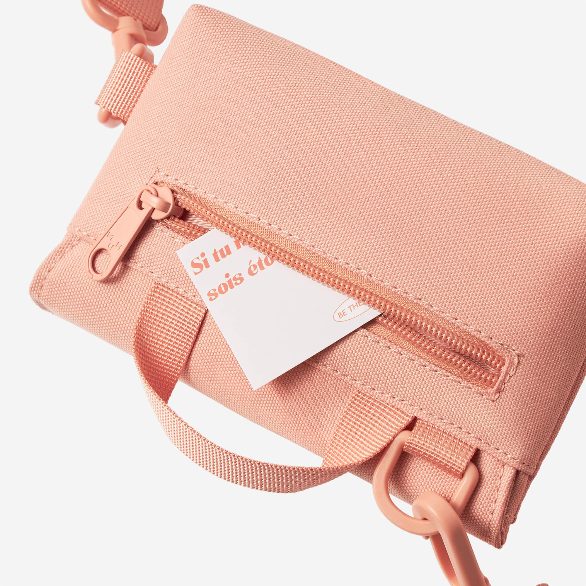 Pink crossbody bag with zipper pocket, adjustable strap, and French text tag