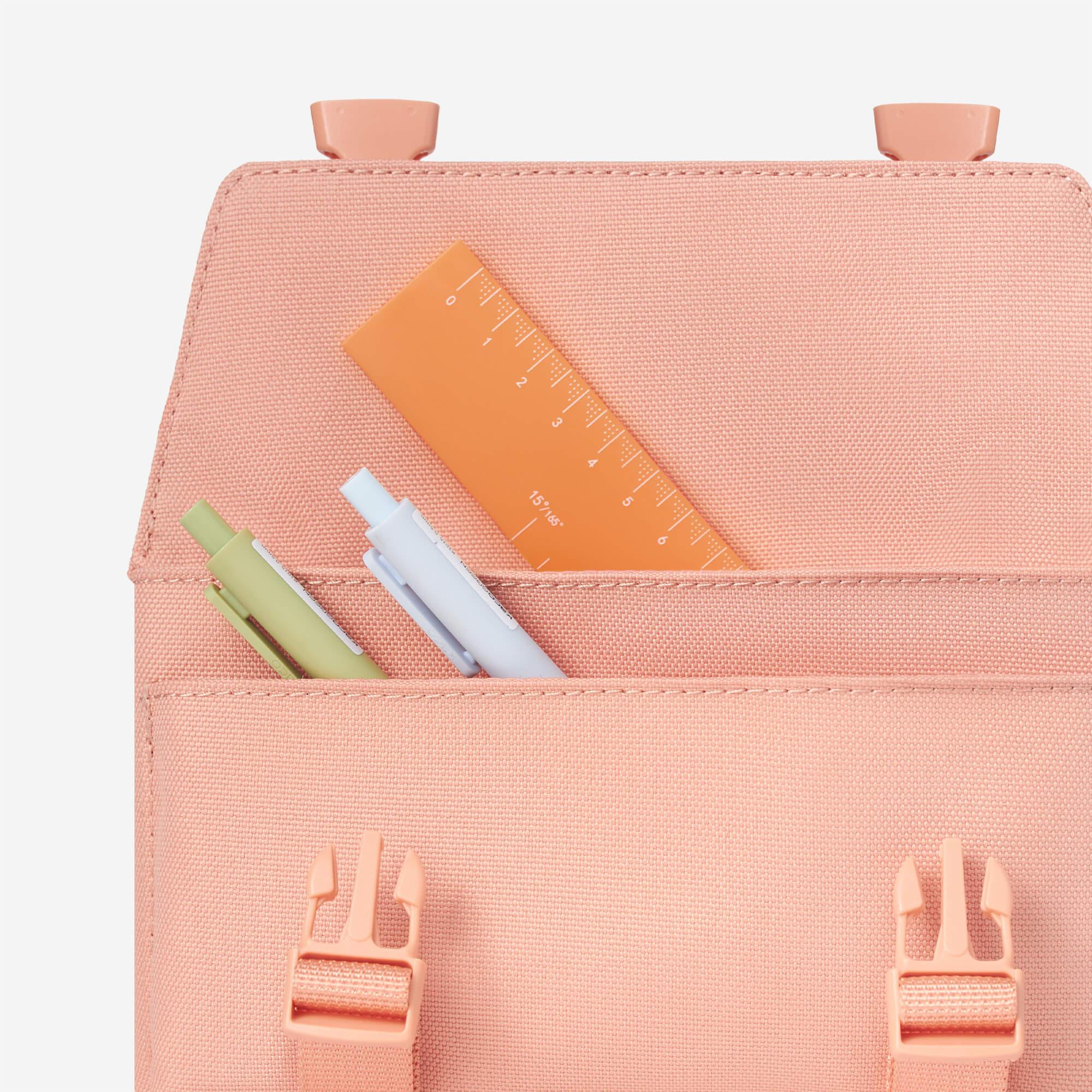 Peach canvas backpack front pocket holding pens and ruler, ideal for school or daily use