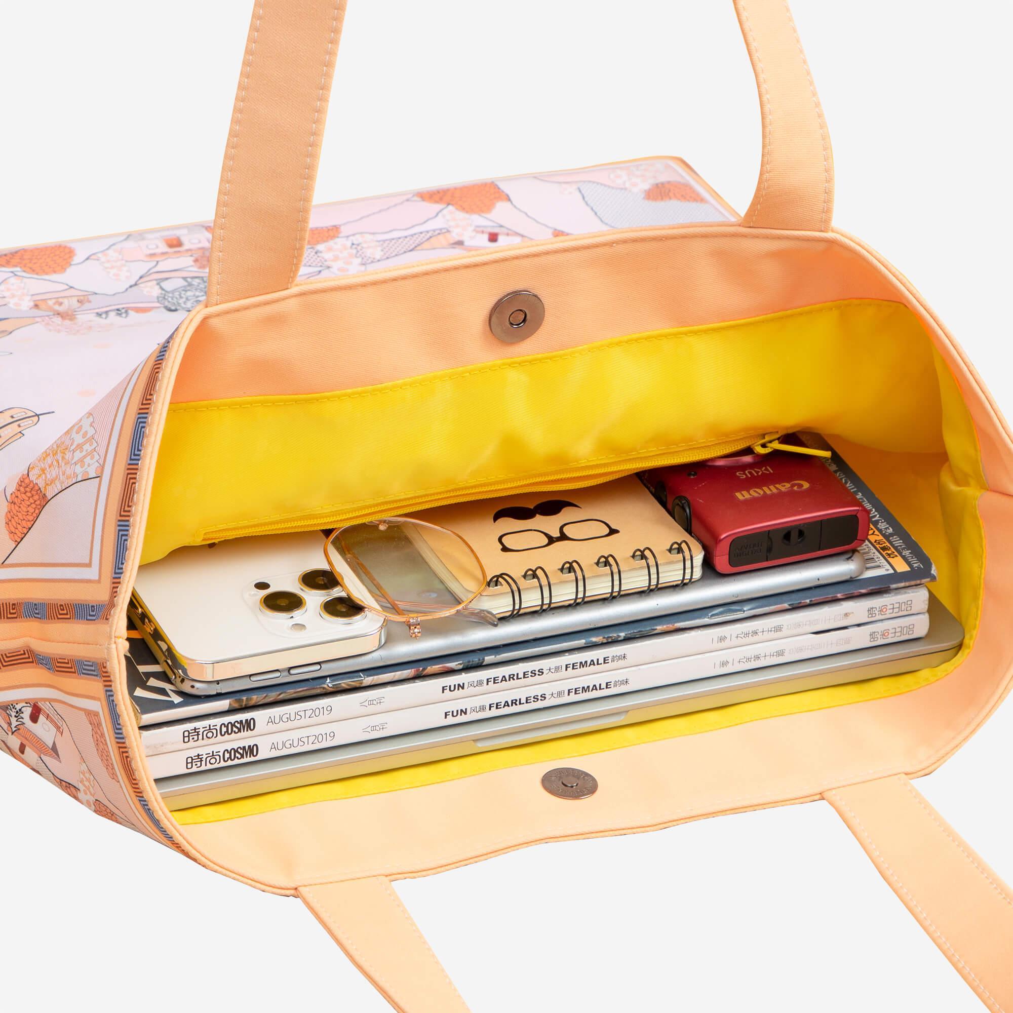 Stylish tote bag with floral print, holding phone, camera, notebooks, and magazines, perfect for daily essentials.