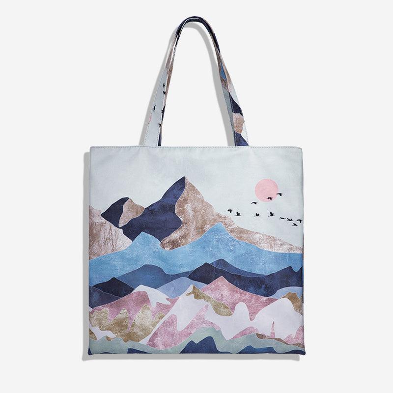 Stylish tote bag with abstract mountain landscape print, pink sun, and flying birds, ideal for everyday use.