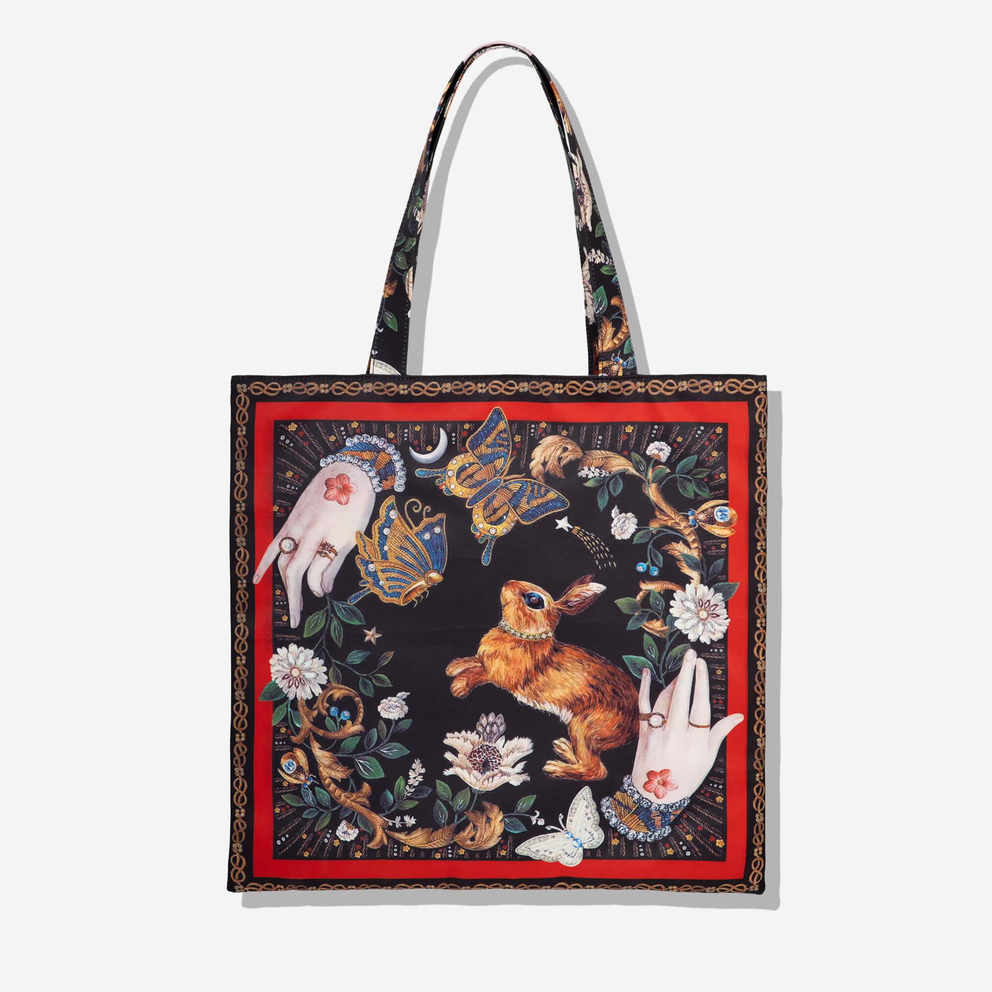 Artistic tote bag with rabbit, butterflies, floral design, and hands on black background, red border
