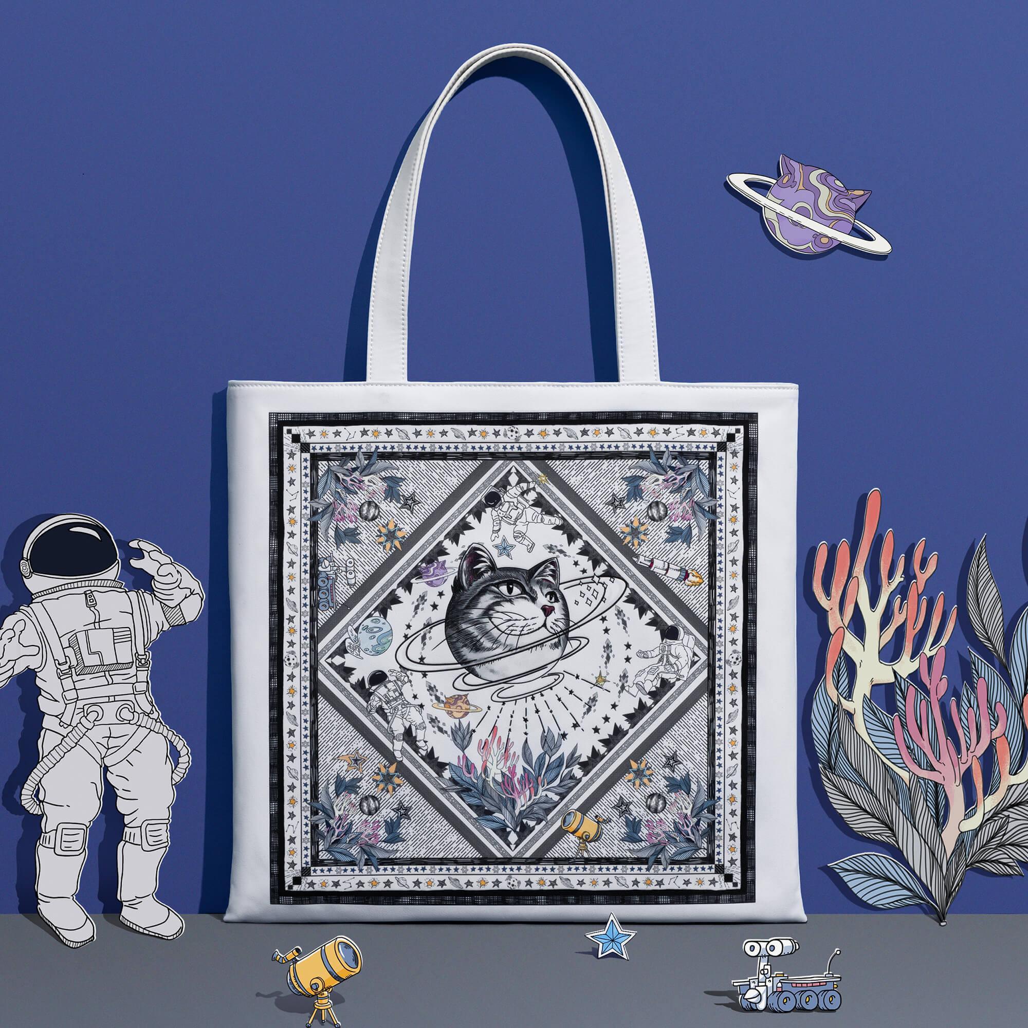 White tote bag with cat in space design, astronaut, planets, and coral accents on blue background