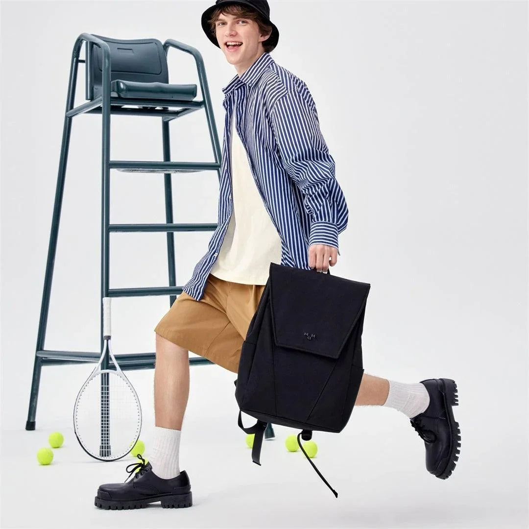 Man holding black backpack with tennis racket and balls, stylish everyday bag for active lifestyle
