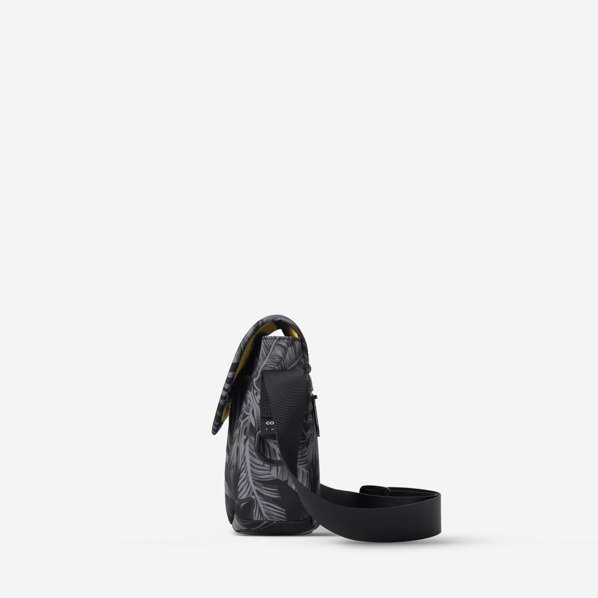 Black crossbody bag with gray leaf print and yellow interior, featuring adjustable strap and front pocket