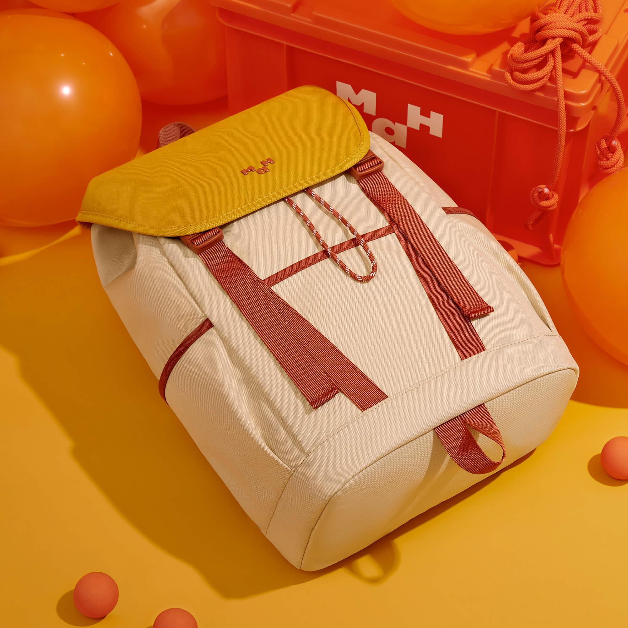 Cream backpack with mustard flap and red straps, styled with orange balloons and storage crate