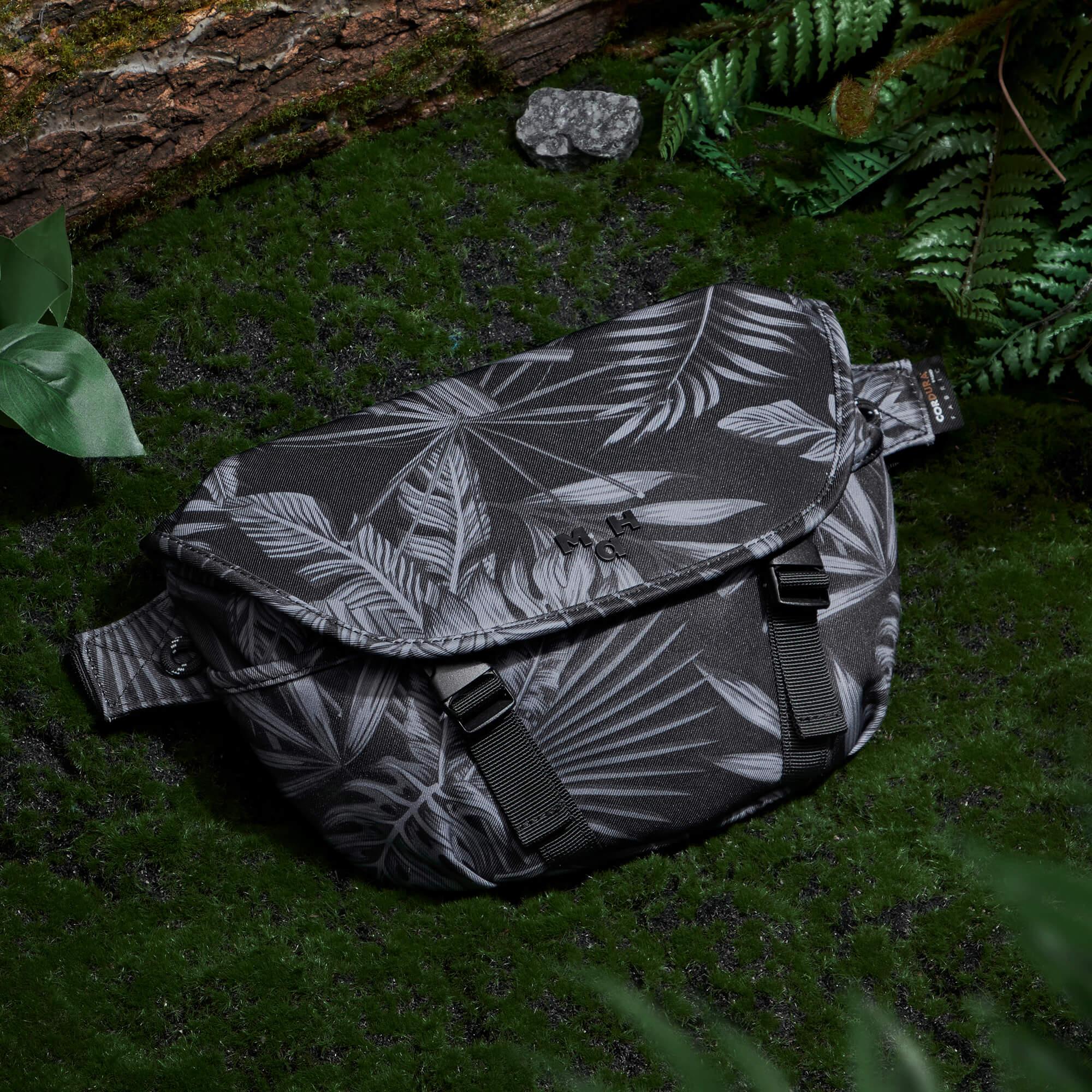 Black and white leaf print sling bag on mossy forest floor with ferns and log