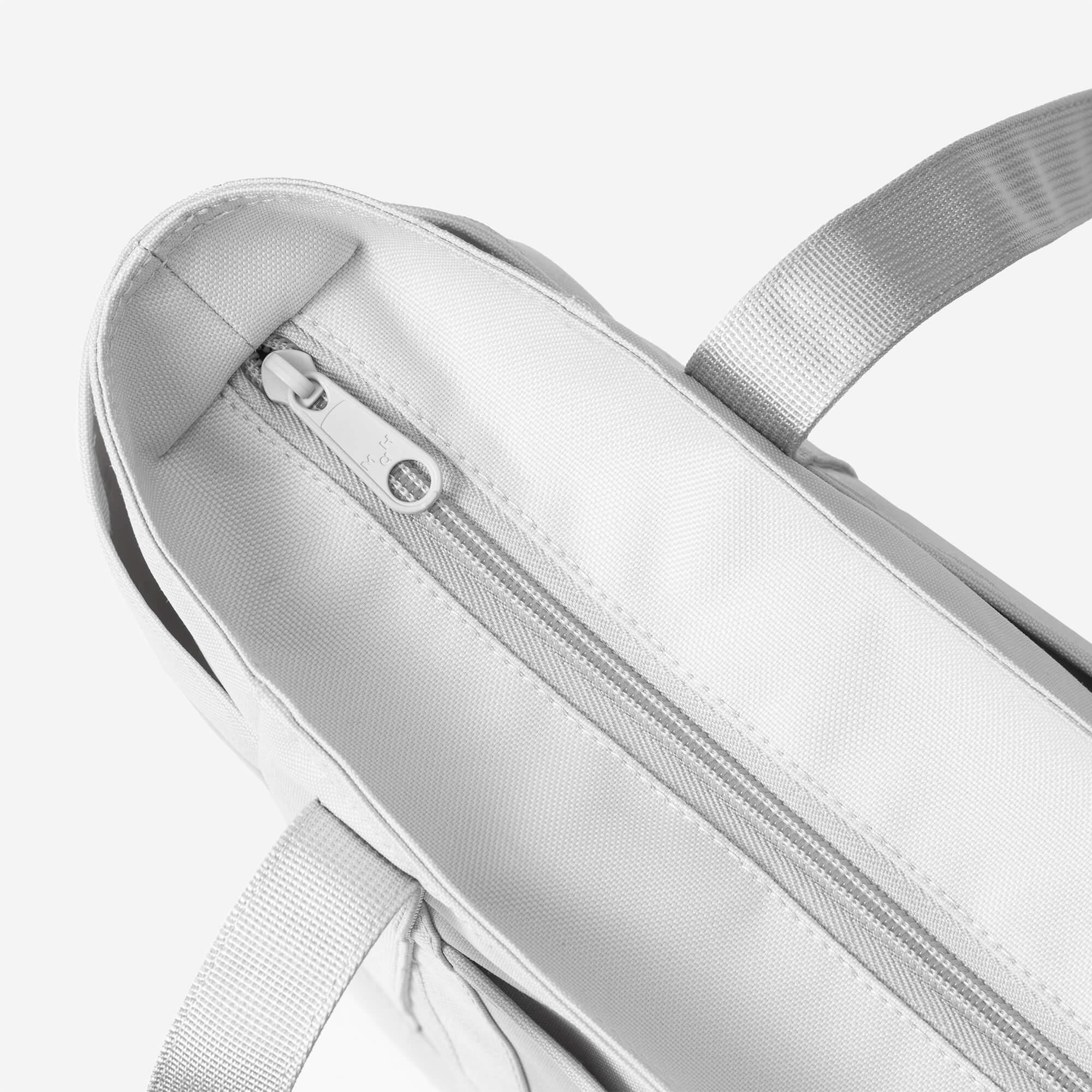 Light gray tote bag with zipper closure and sturdy handles, ideal for everyday carry and lifestyle use.