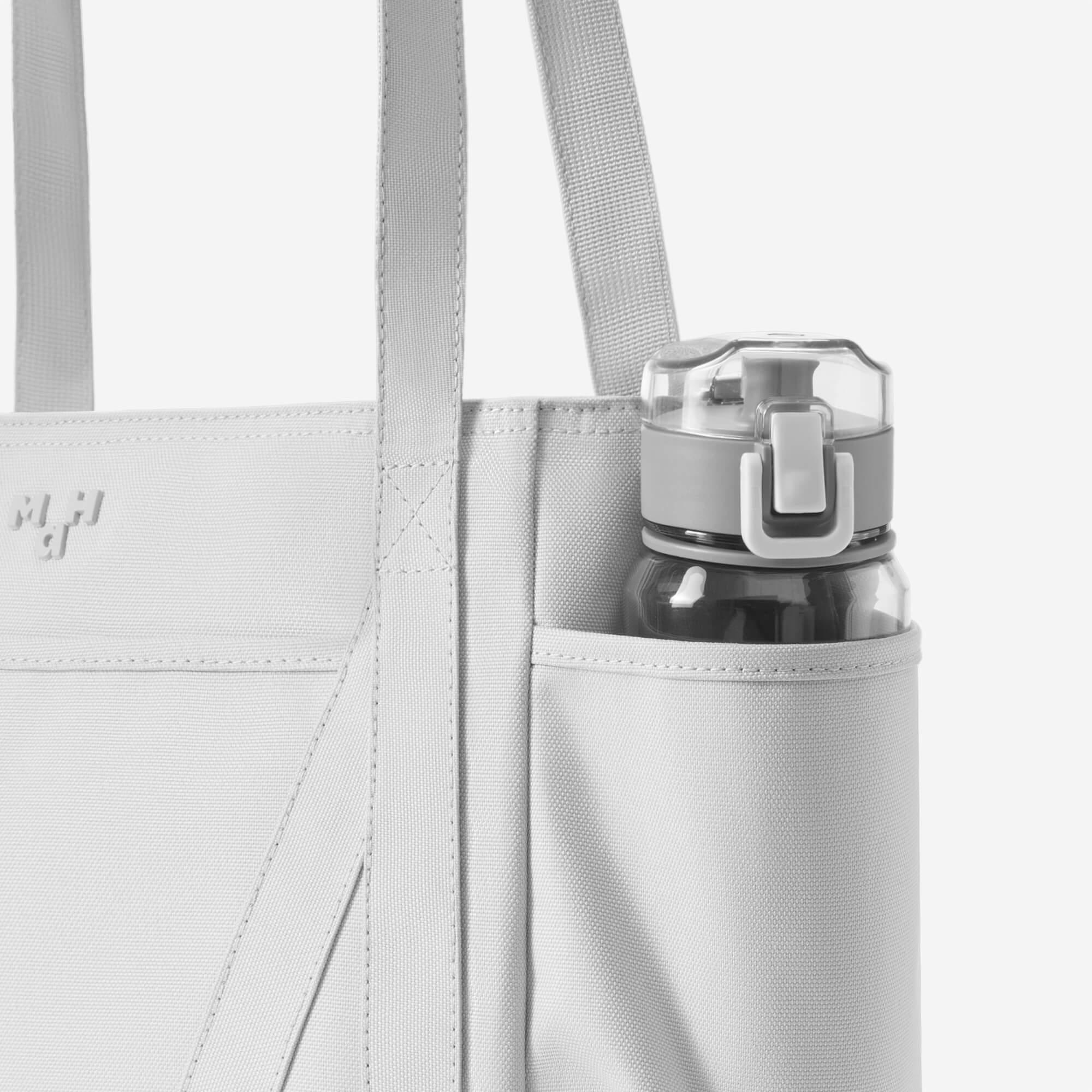 Light gray tote bag with side water bottle pocket and subtle logo, ideal for daily carry and hydration on the go.