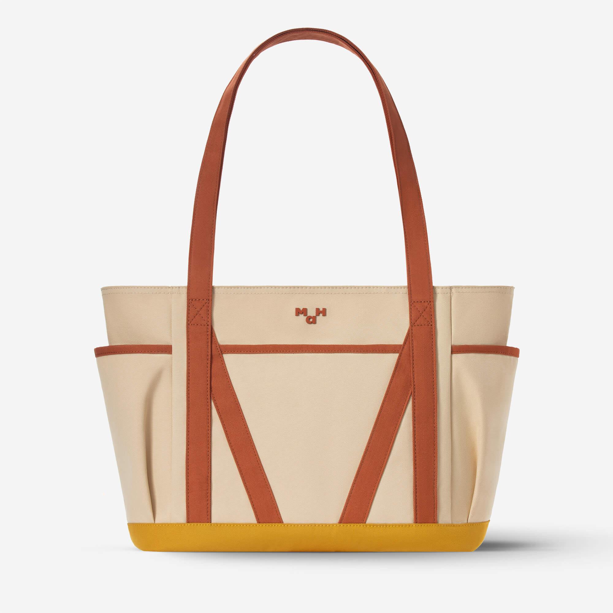 Beige canvas tote bag with brown straps and yellow base, featuring side pockets and minimalist design