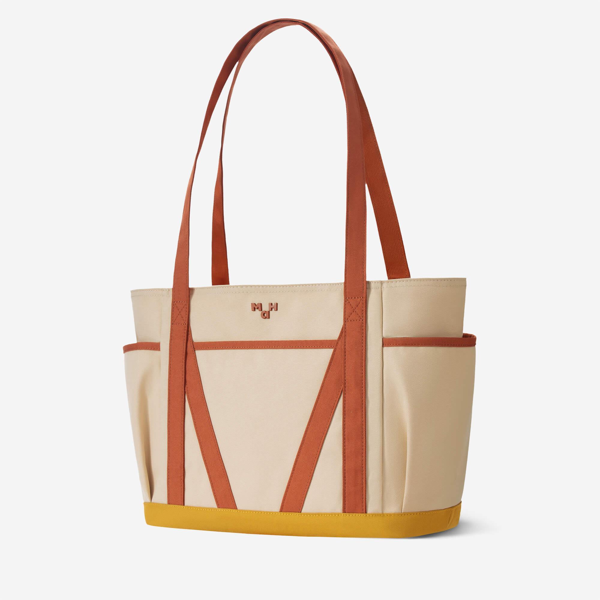 Beige canvas tote bag with rust straps and yellow base, featuring front pockets and minimalist design