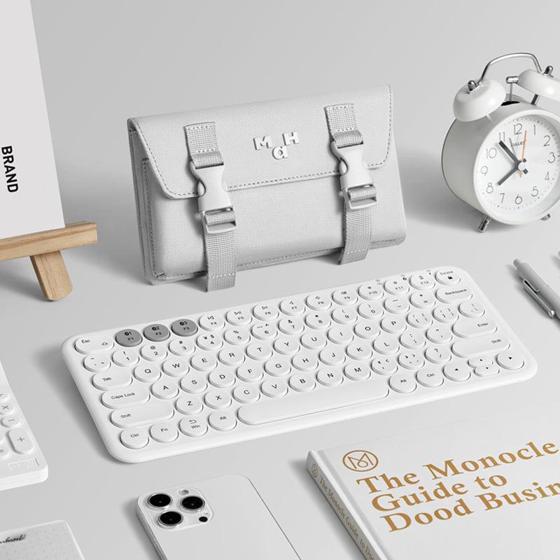 Minimalist white desk setup with compact keyboard, sleek pouch, alarm clock, and Monocle business guide