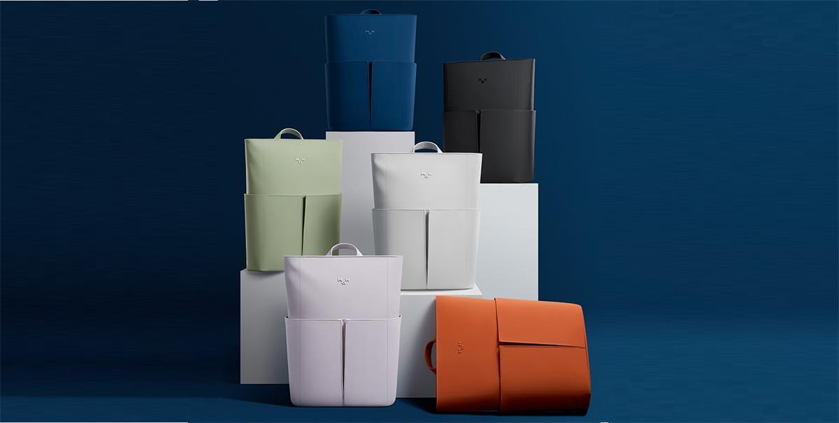 Minimalist backpacks in blue, green, white, black, and orange on display stands