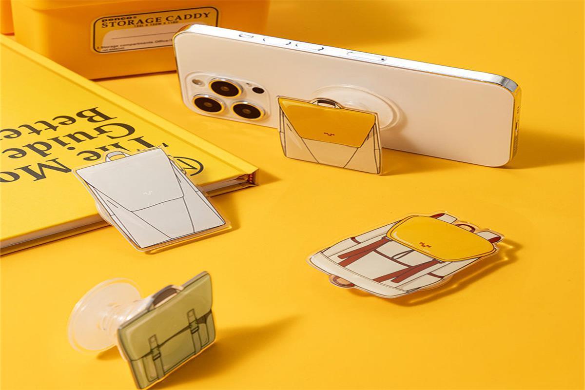 Cute bag-shaped phone grips with suction stands, stylish accessories for smartphones on yellow desk
