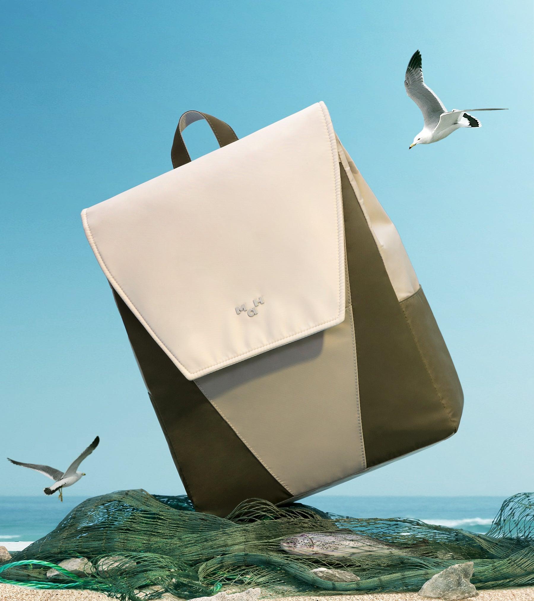 Cream and olive backpack on beach with seagulls, fishing net, and ocean backdrop