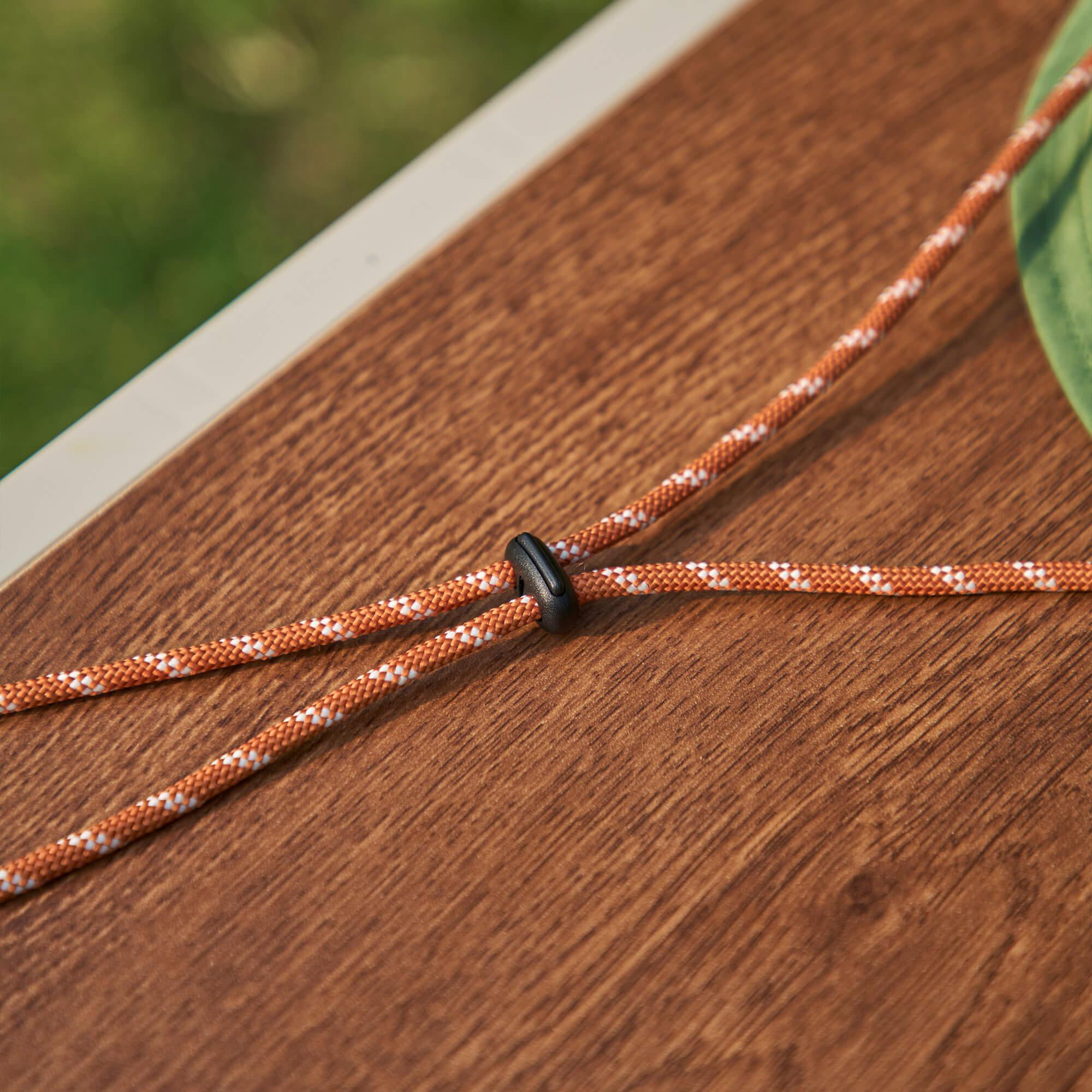 Orange and white braided drawstring with black toggle on wooden surface, ideal for backpacks and bags
