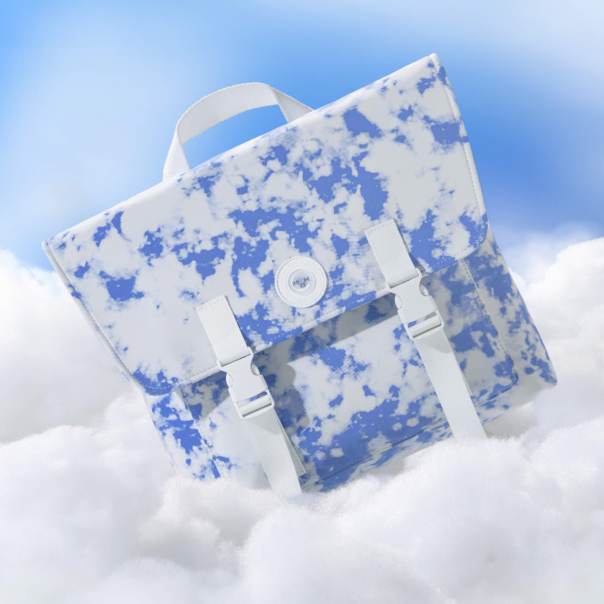 Blue and white cloud-print backpack with white straps, set against sky and clouds