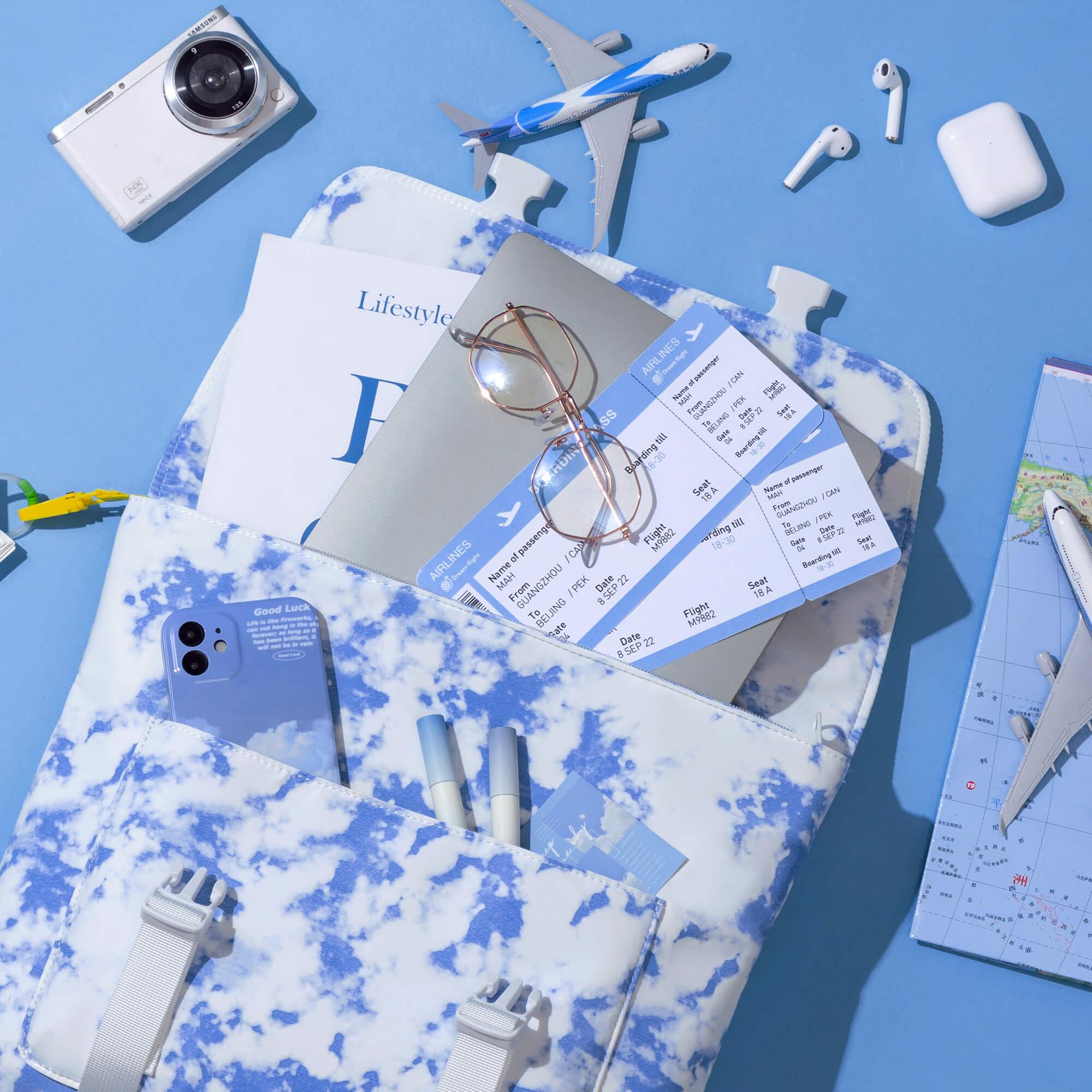 Cloud-print travel organizer with boarding passes, phone, glasses, and accessories on blue background