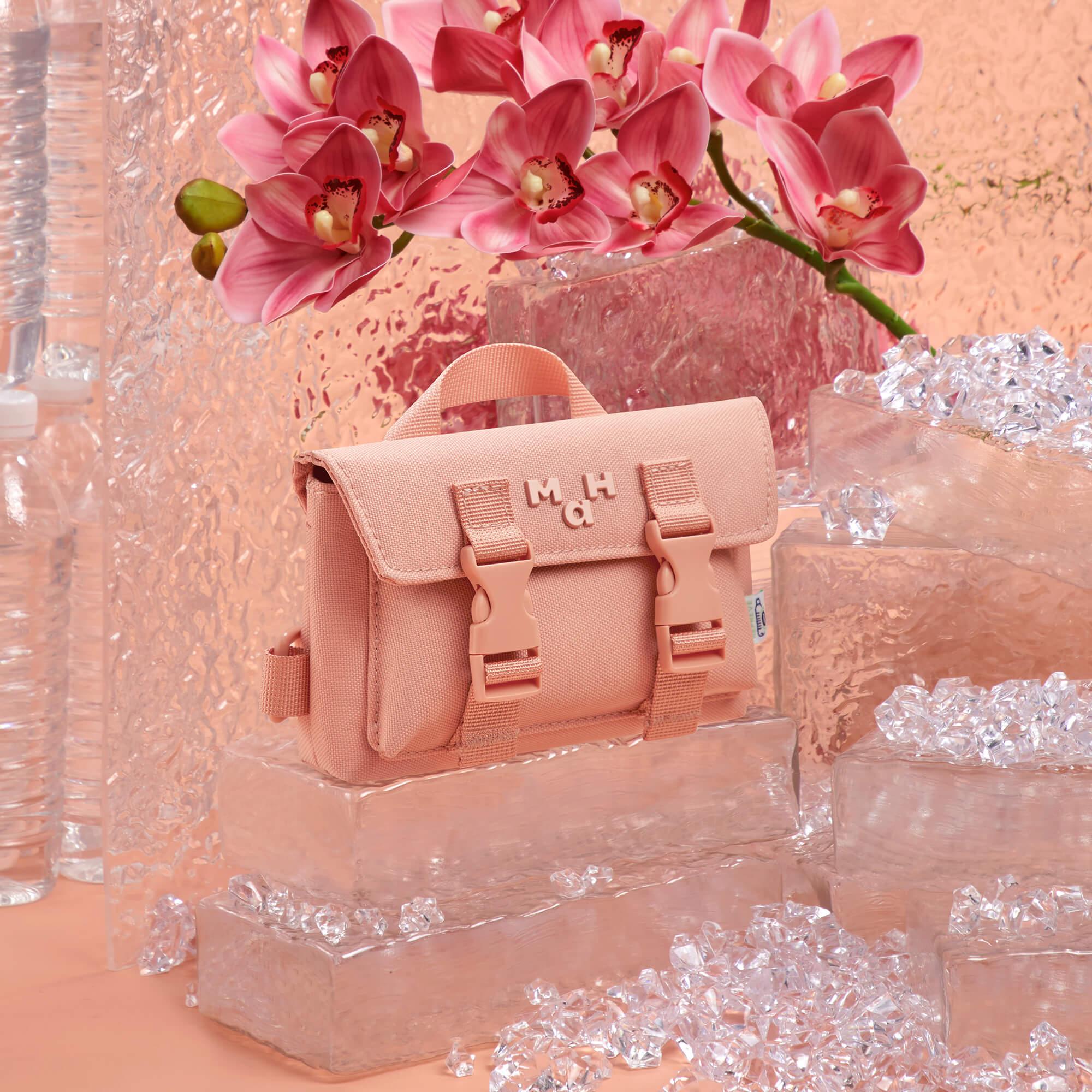 Pink canvas crossbody bag with buckle straps, displayed on ice blocks with pink orchids