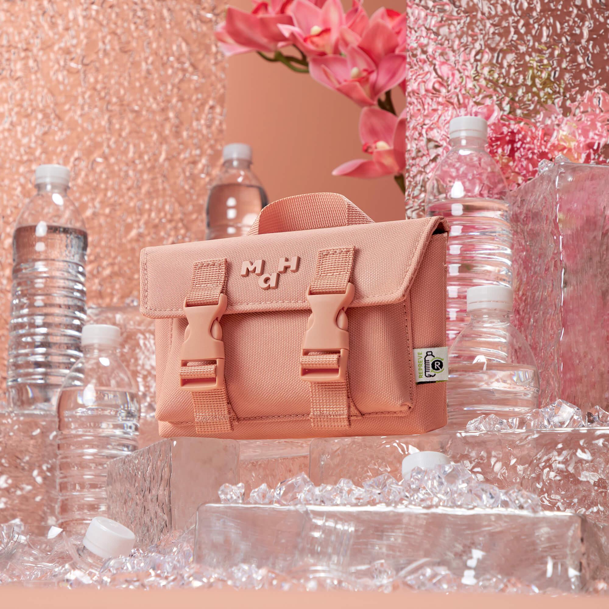 Pink canvas lunch bag with buckles, surrounded by water bottles and ice, ideal for daily use or picnics.