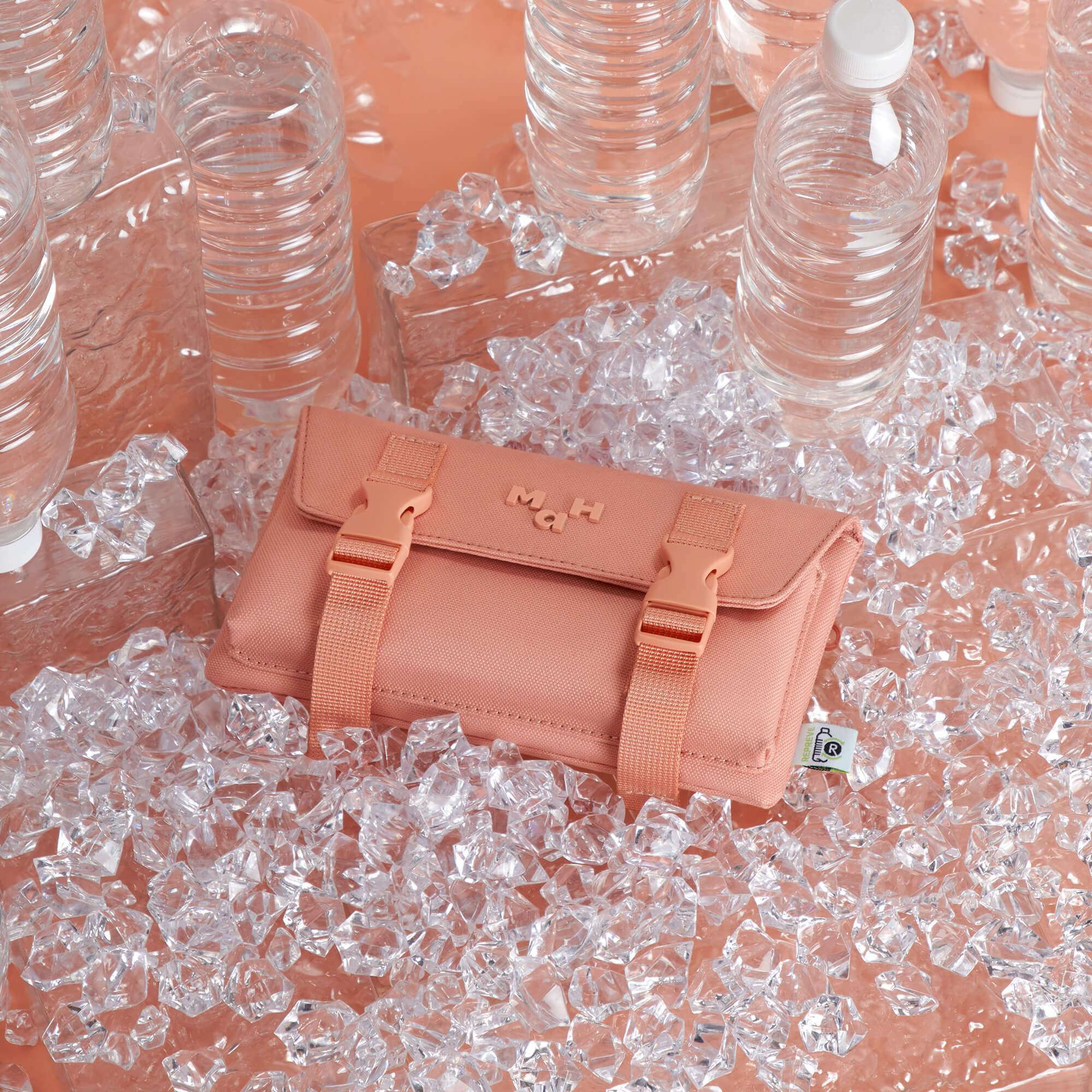 Pink MaH recycled accessory pouch with buckle straps, surrounded by plastic bottles and ice crystals