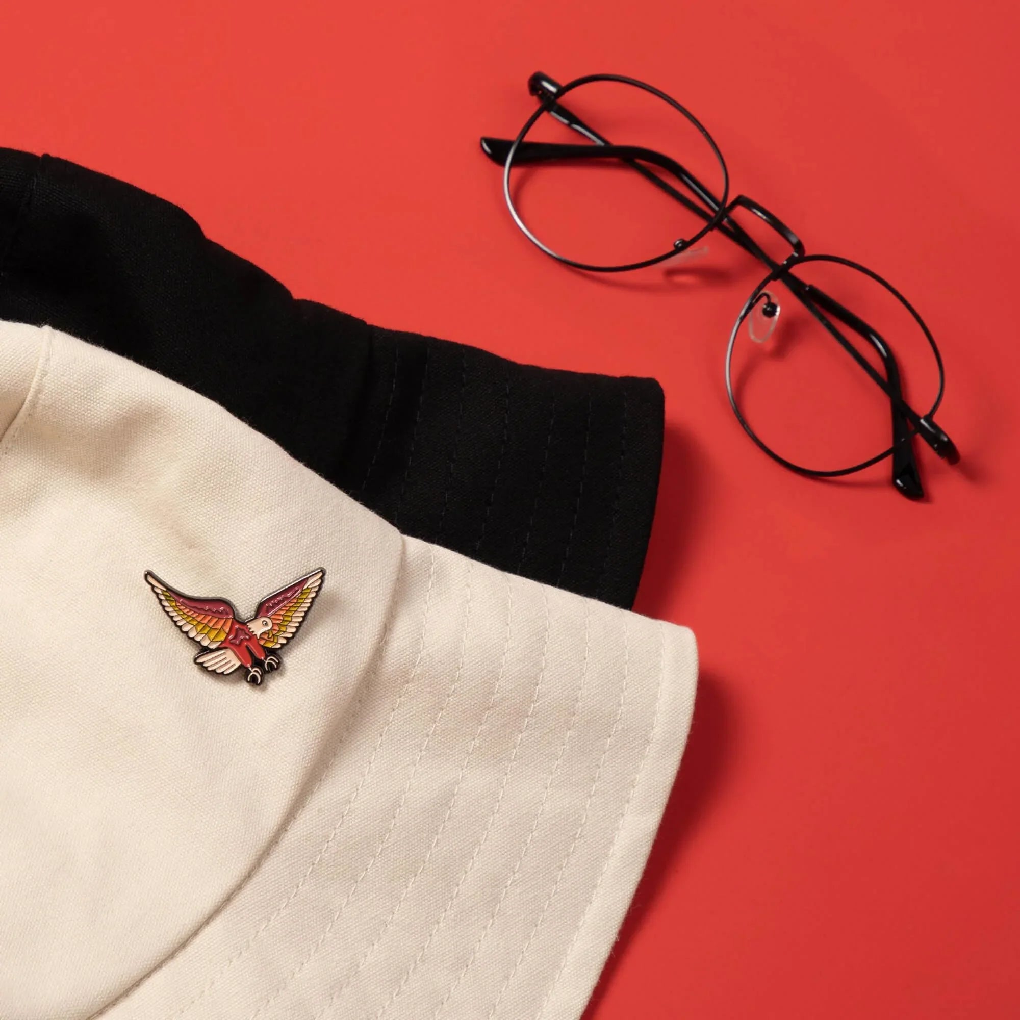 Colorful bird enamel pin on beige cap with black band, styled with glasses on red background