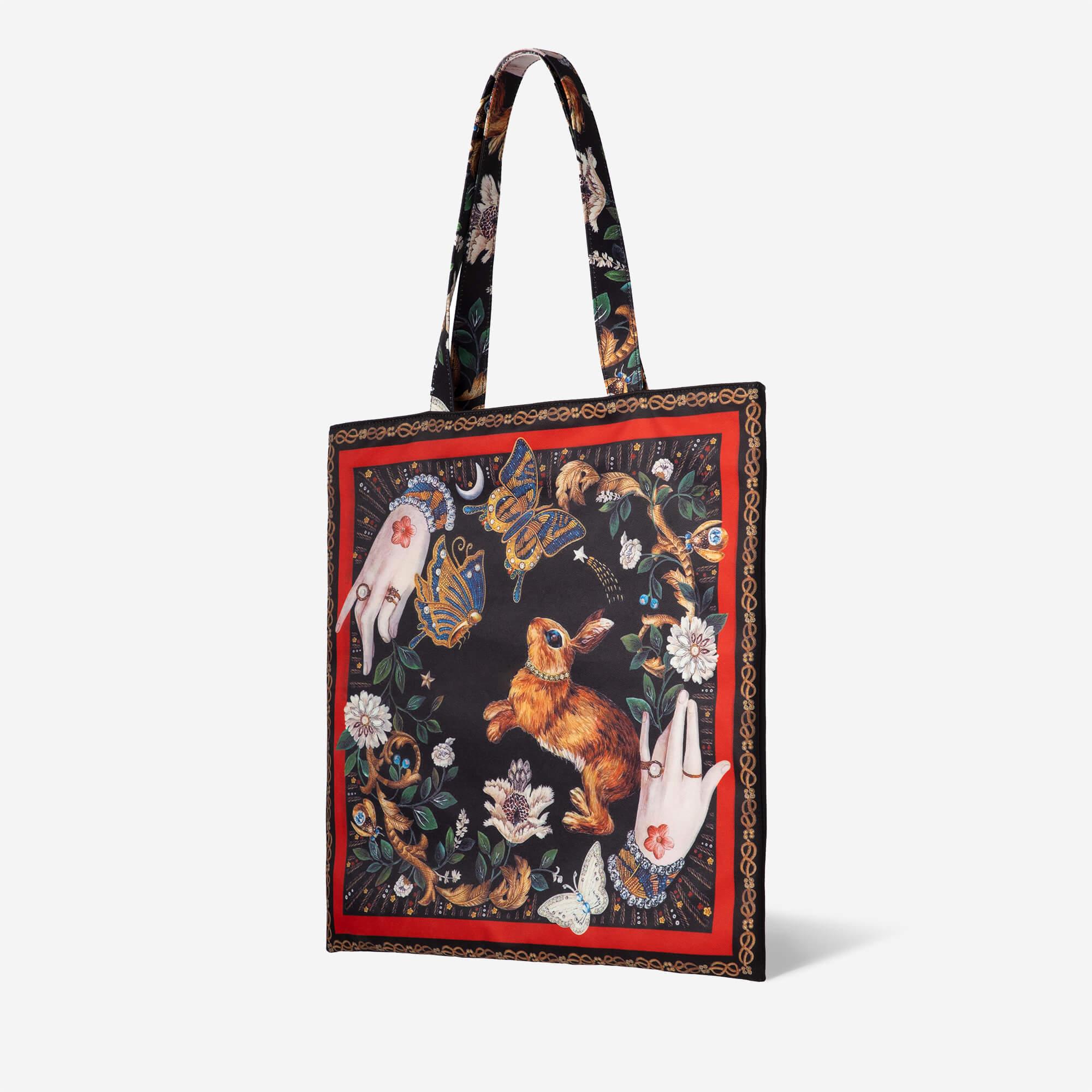 Fantasy tote bag with rabbit, butterflies, hands, and floral art on black background