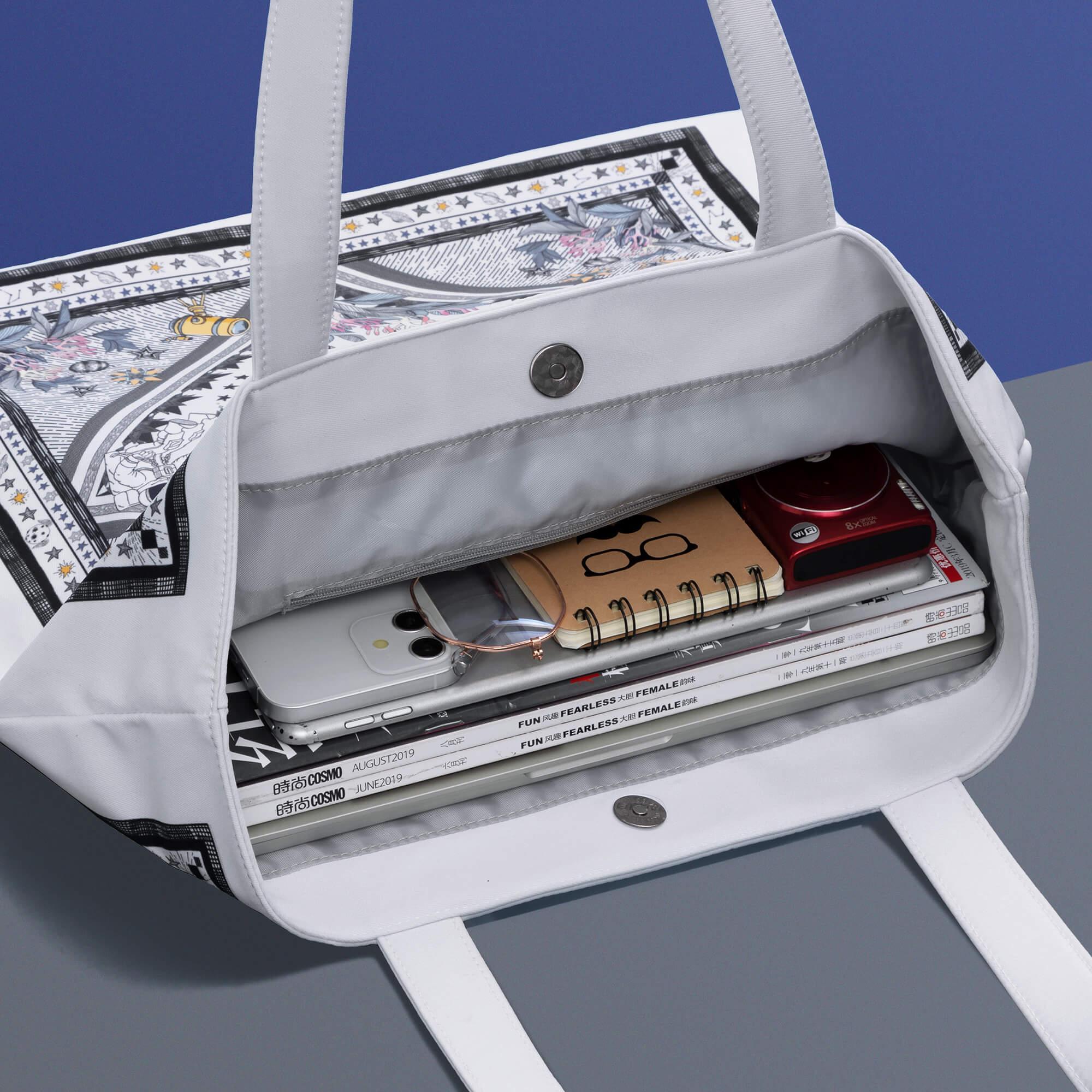 White tote bag with star print, holding phone, notebook, camera, and magazines, ideal for daily use and travel.