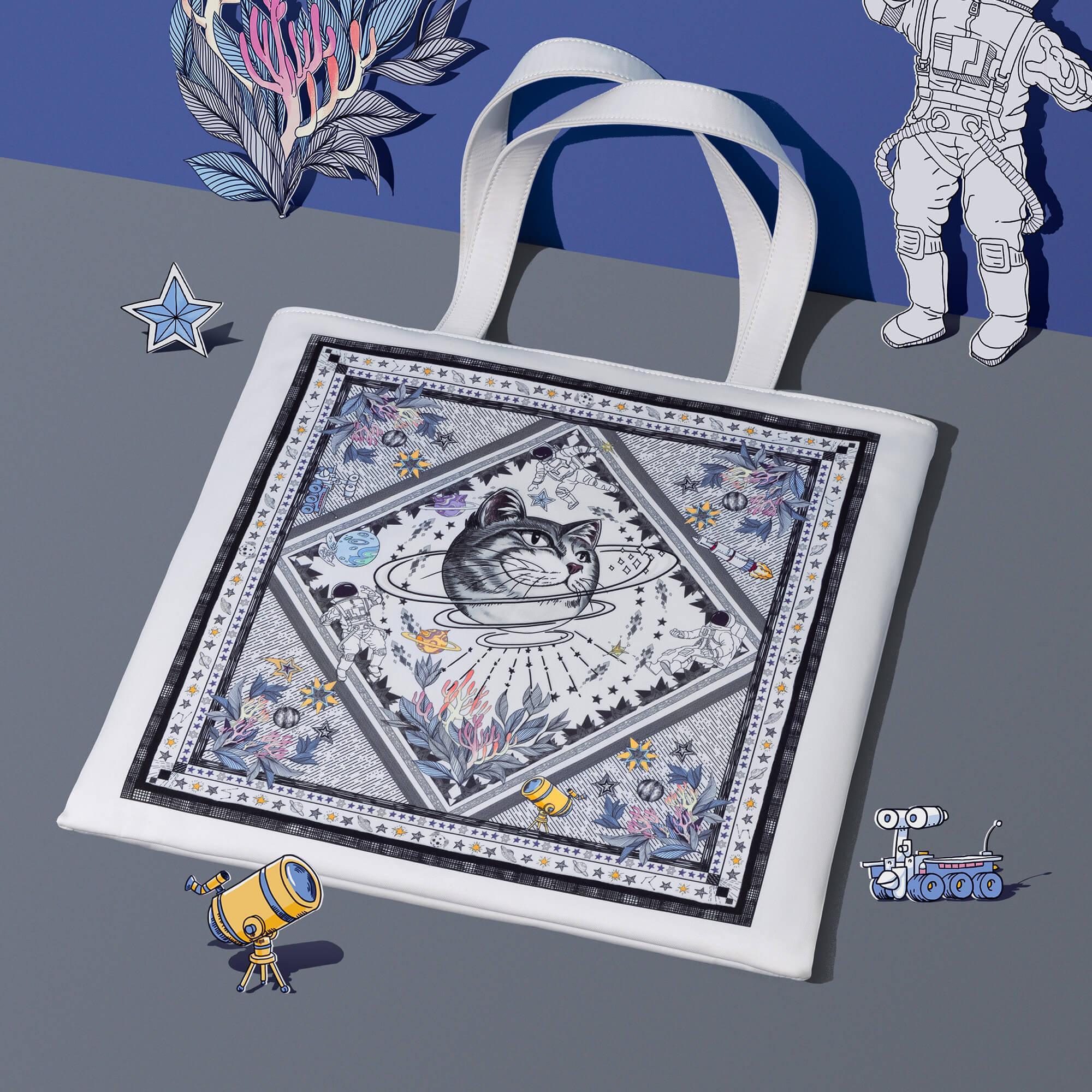 White tote bag with whimsical space cat print, astronauts, planets, and floral accents for stylish everyday use.