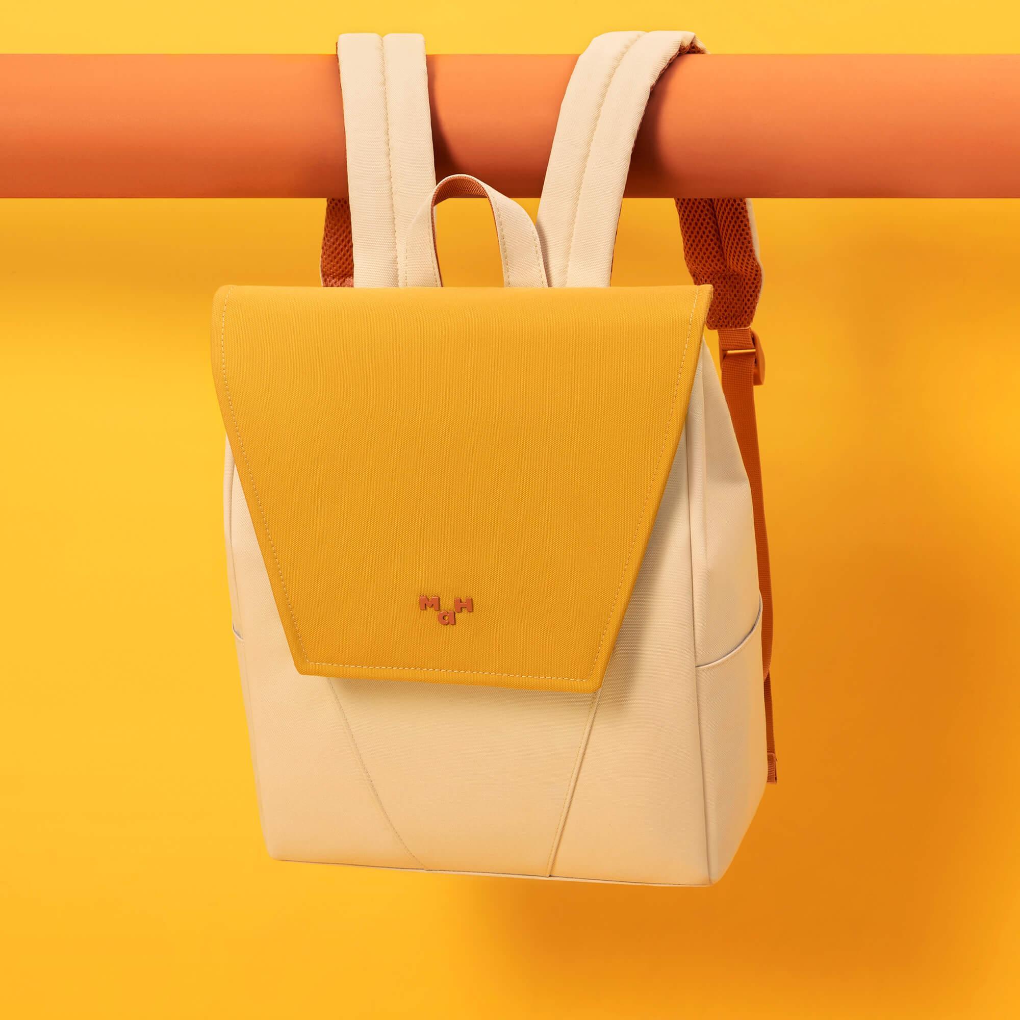 Stylish yellow and cream backpack with minimalist design, hanging on orange bar against vibrant yellow background
