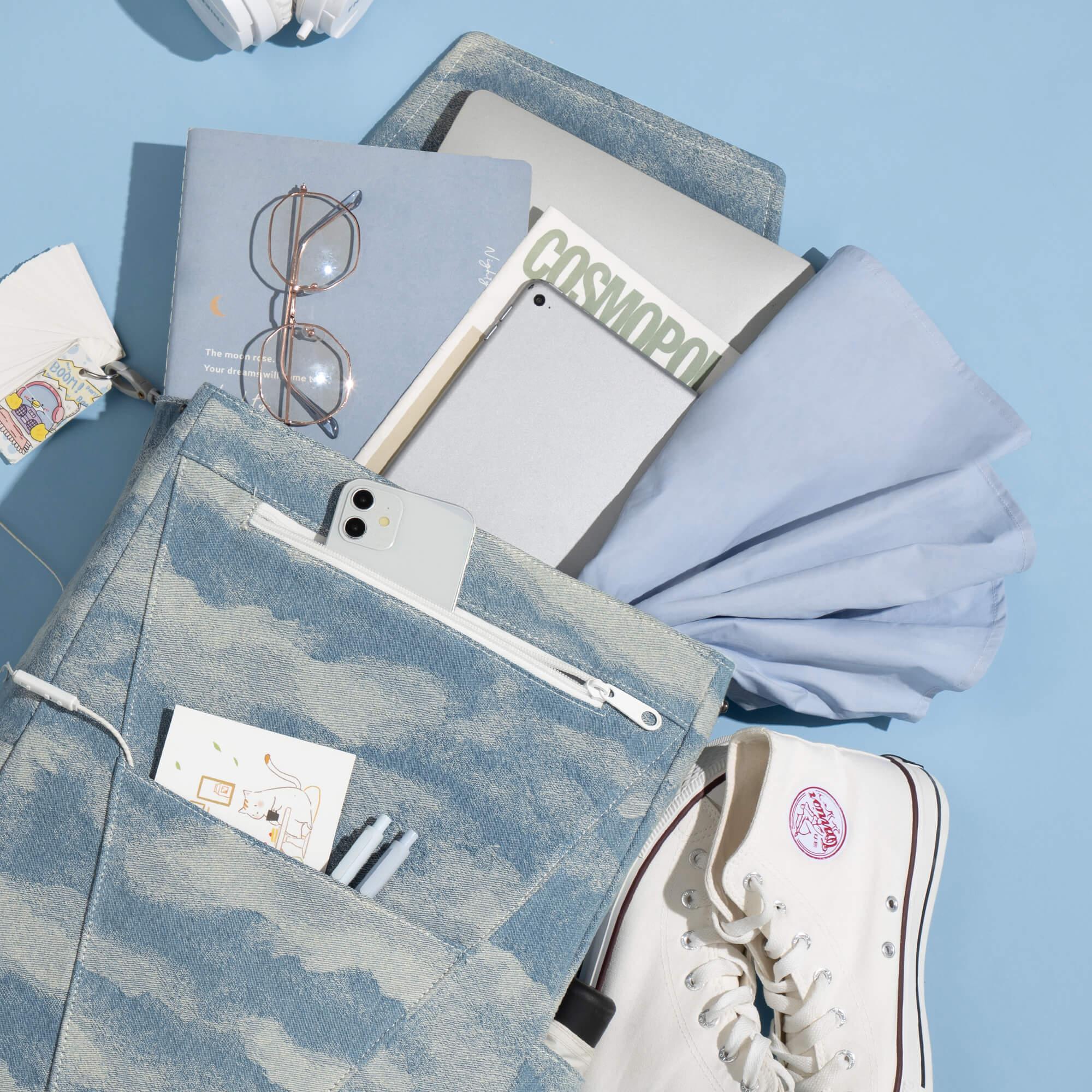 Denim backpack with laptop, phone, glasses, and sneakers on blue background