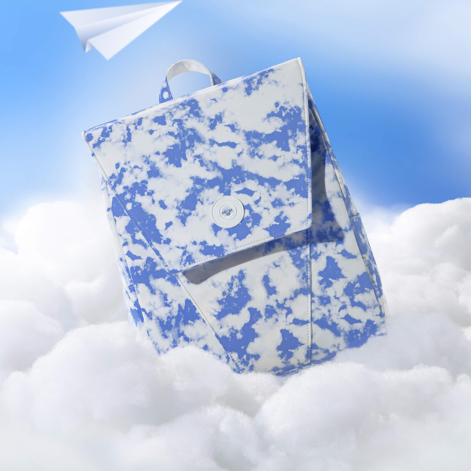 Blue and white cloud-patterned backpack floating on clouds with paper airplane, ideal for travel or school