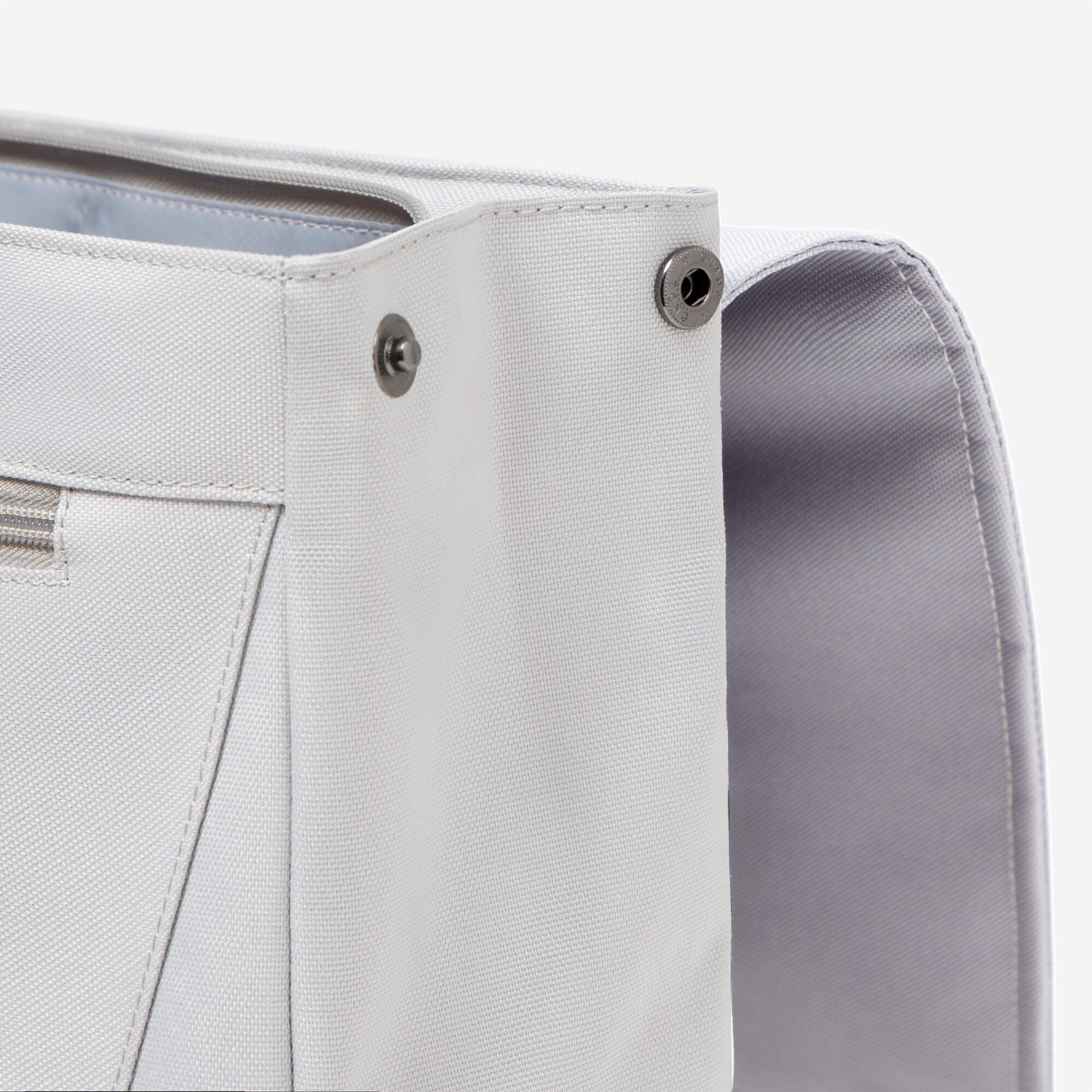 Light gray canvas bag with metal grommets and zipper pocket, durable stitching detail